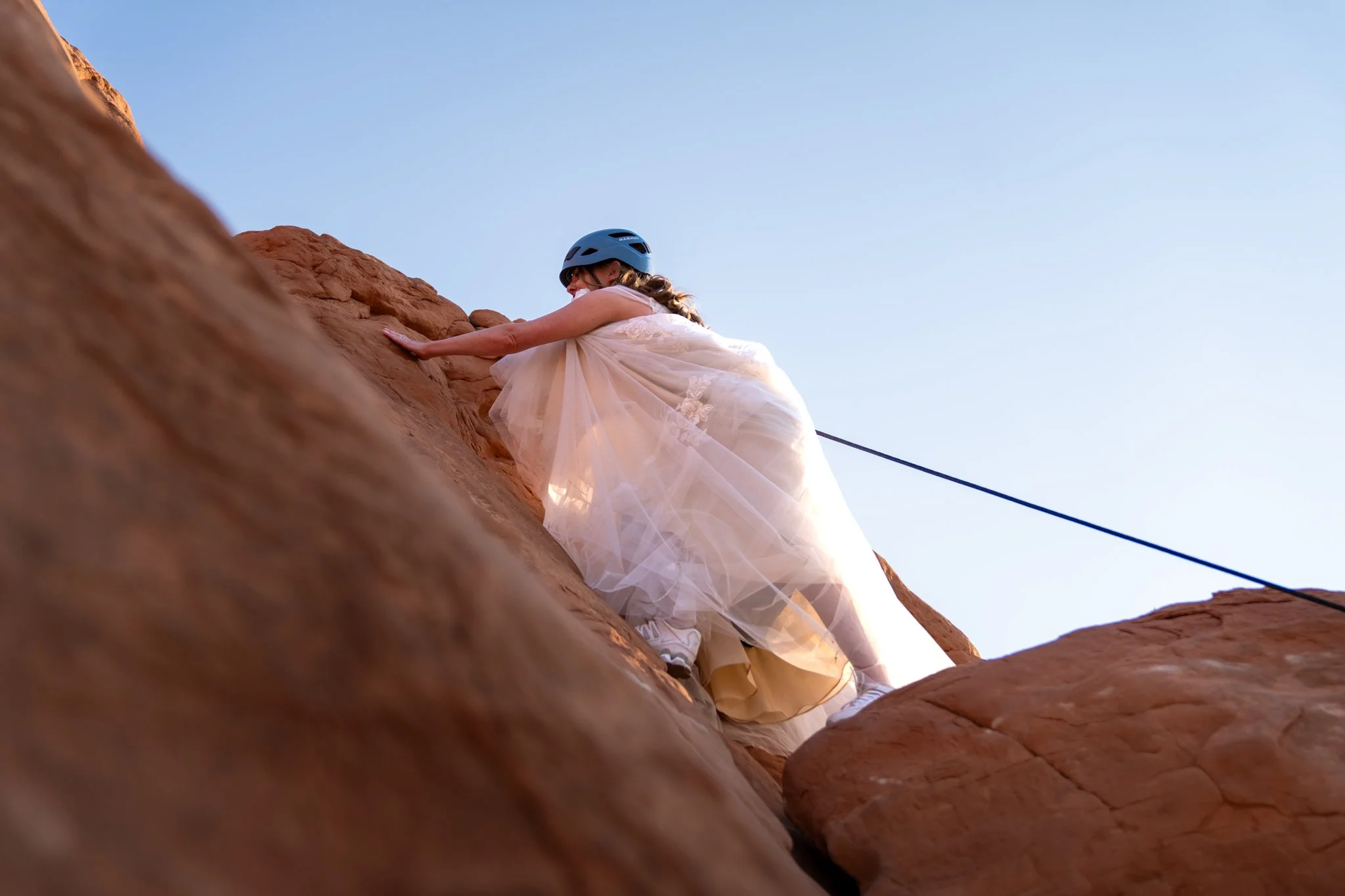 A bride climbs a rock in a wedding dress in Moab.