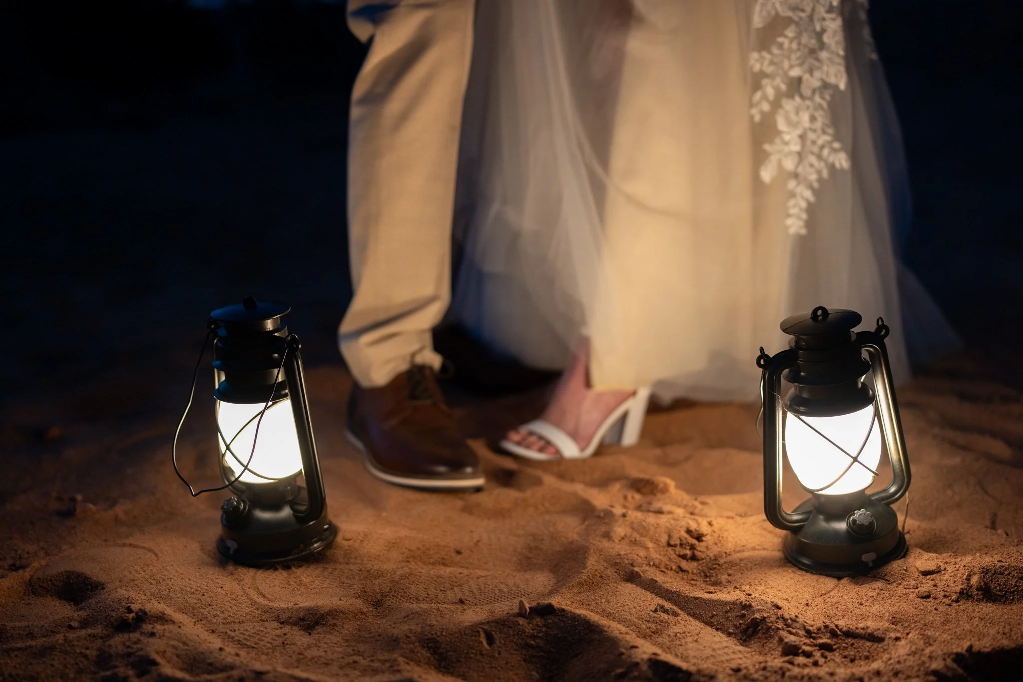 A closeup of the bride and groom's shoes as they stand close together by lantern light.