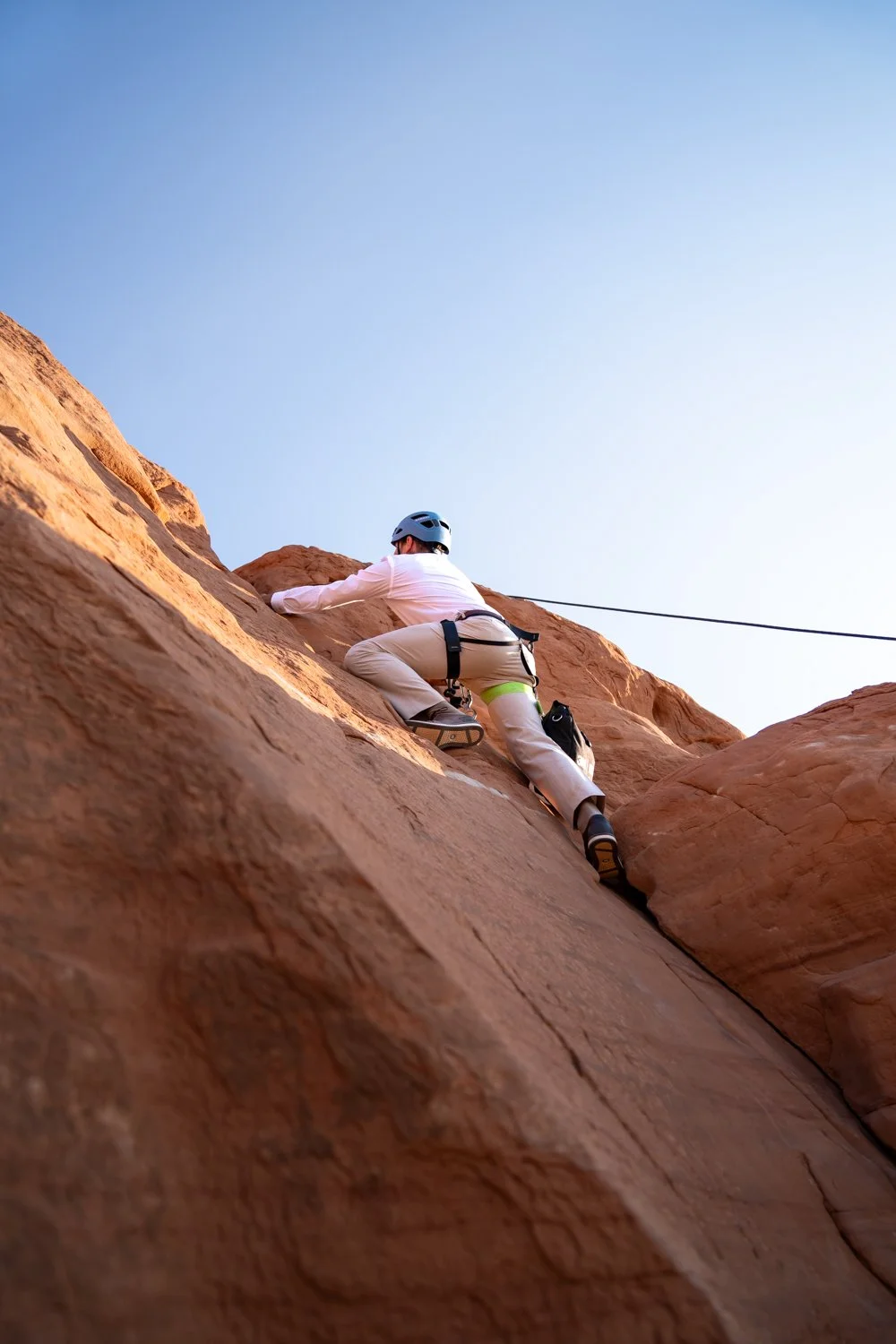 A groom climbs a rock in his wedding suit in Moab.