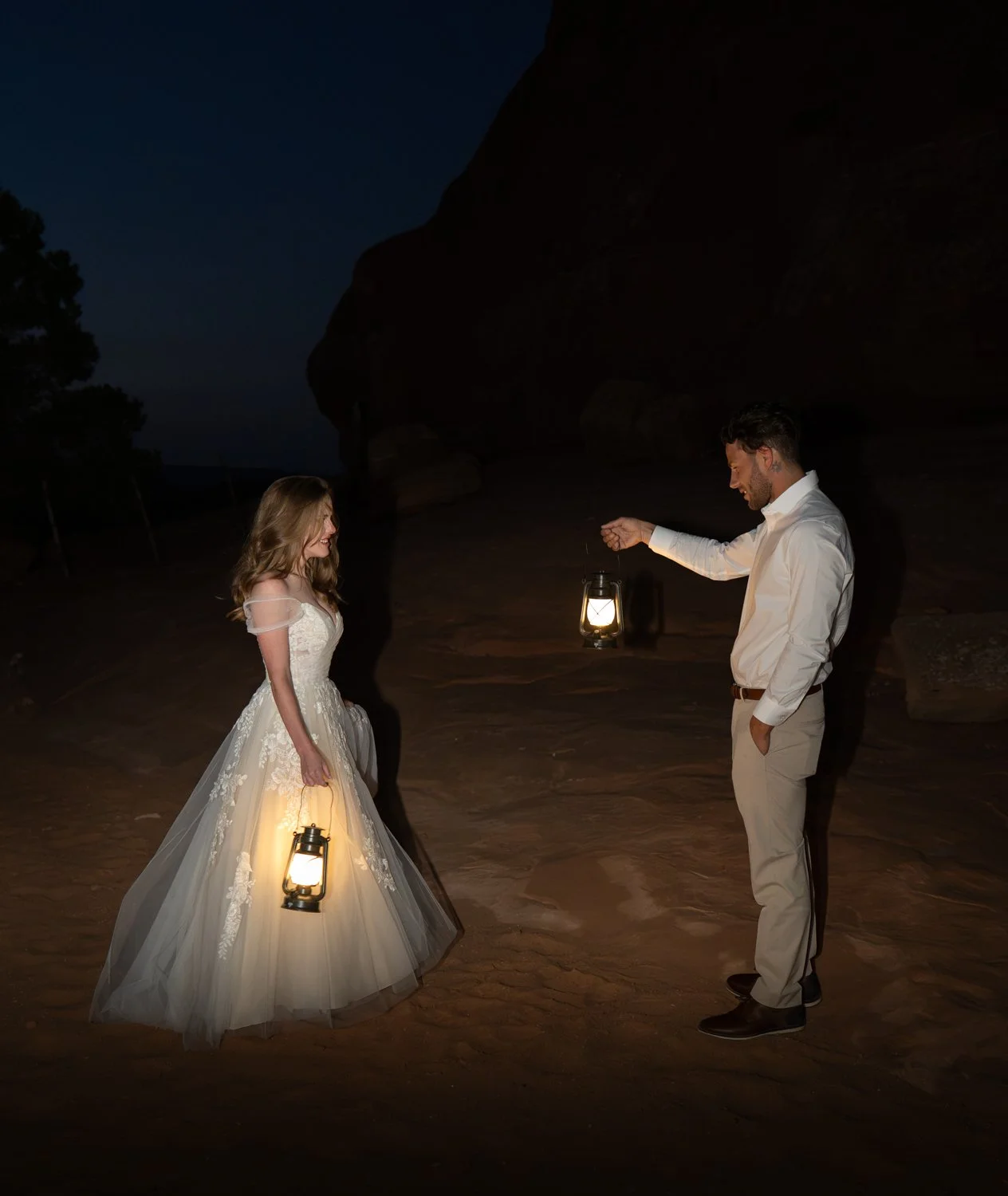 A bride and groom have first looks in the desert dark by lantern light.
