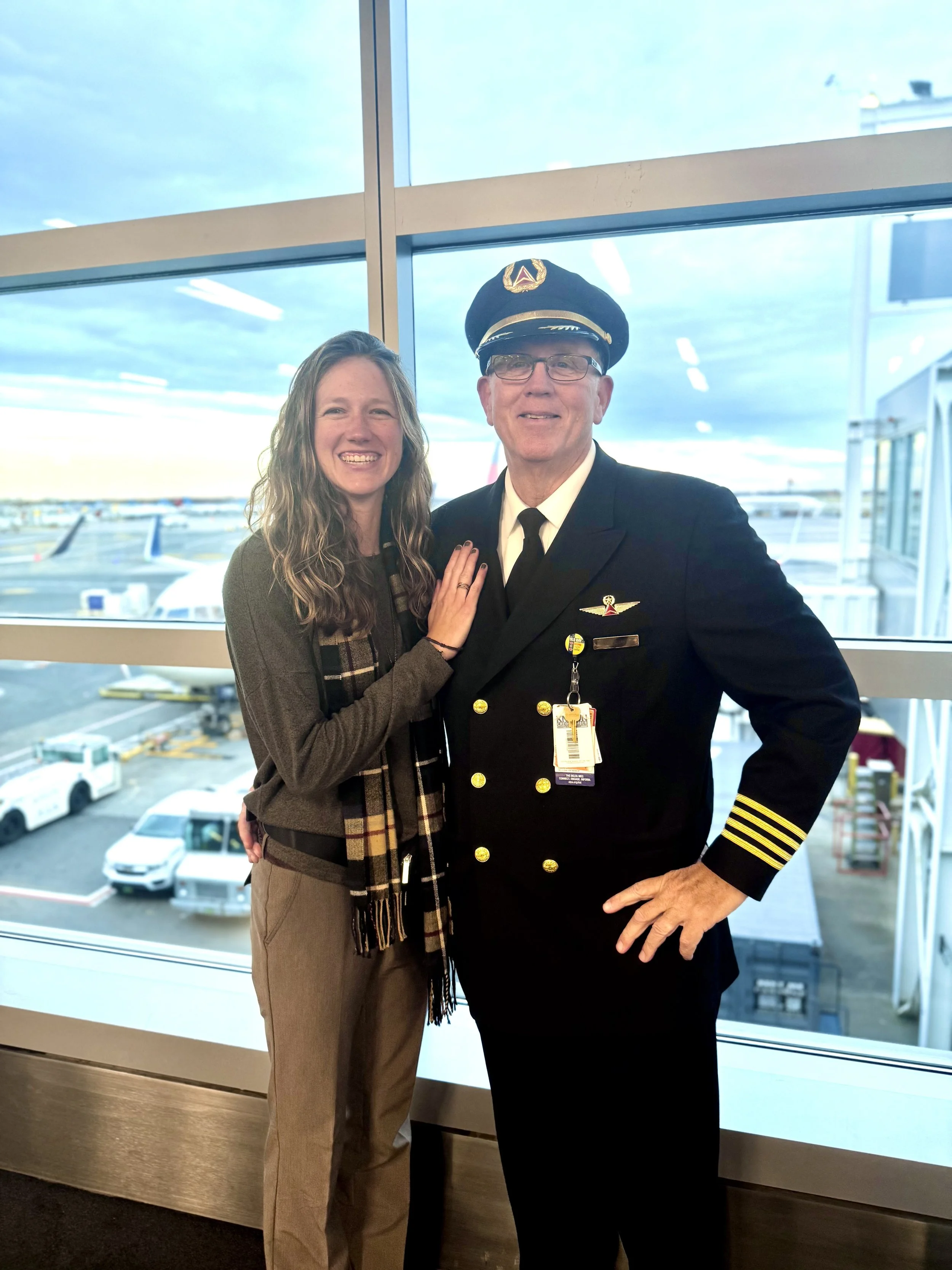 Girl smiling with her dad in his pilot's uniform.