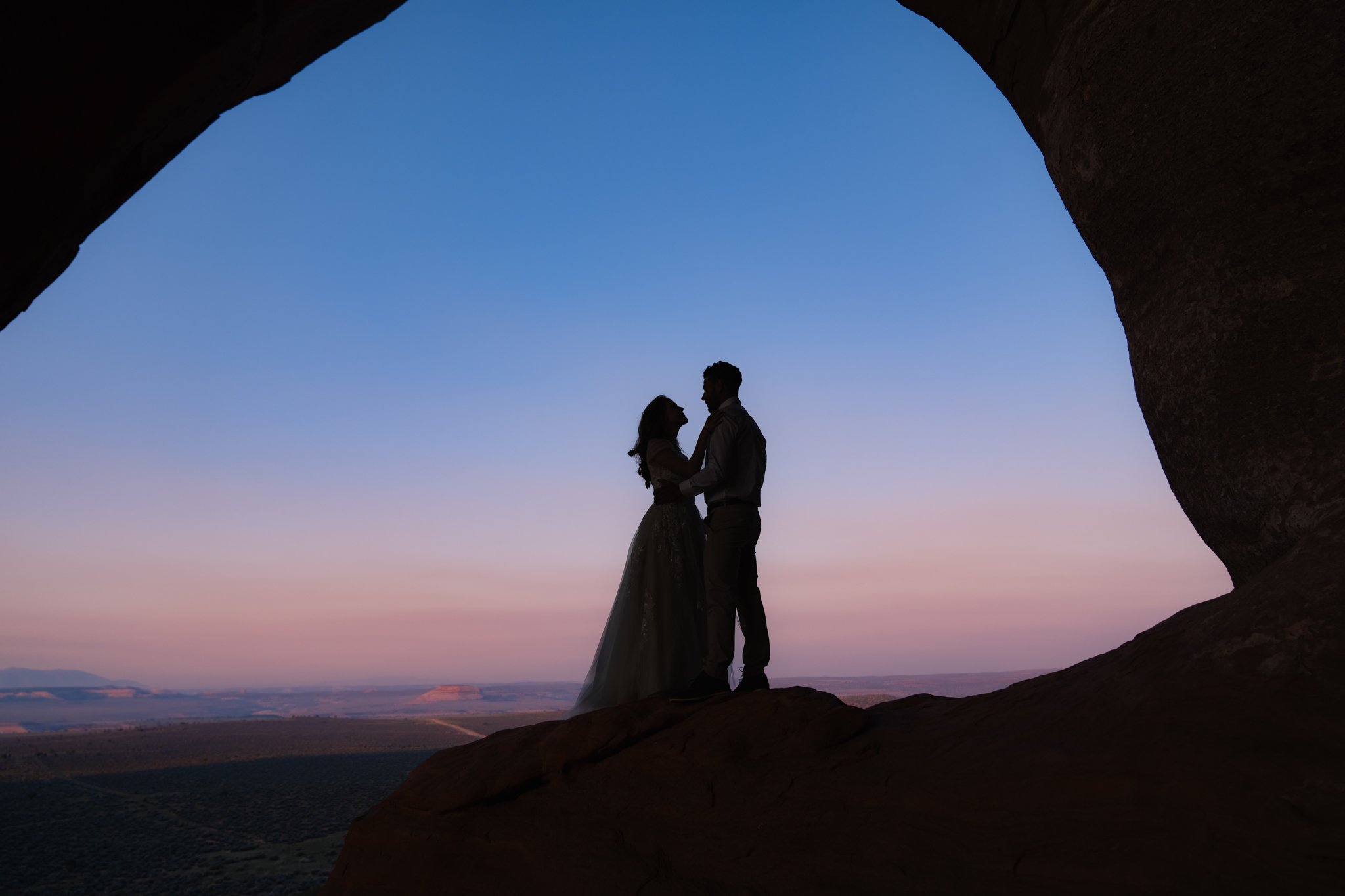A silhouette of a bride and groom in an archway in Moab at sunrise.
