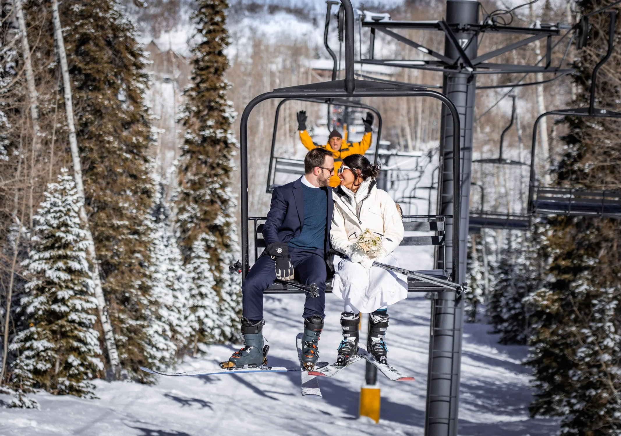 A bride and groom lean in for a kiss on a chair lift at ski resort.