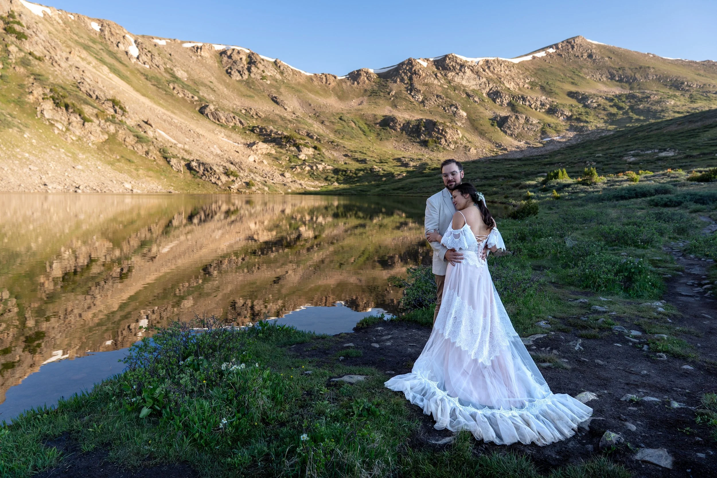 An elopement couple holds each other by an alpine lake at sunrise in Colorado.