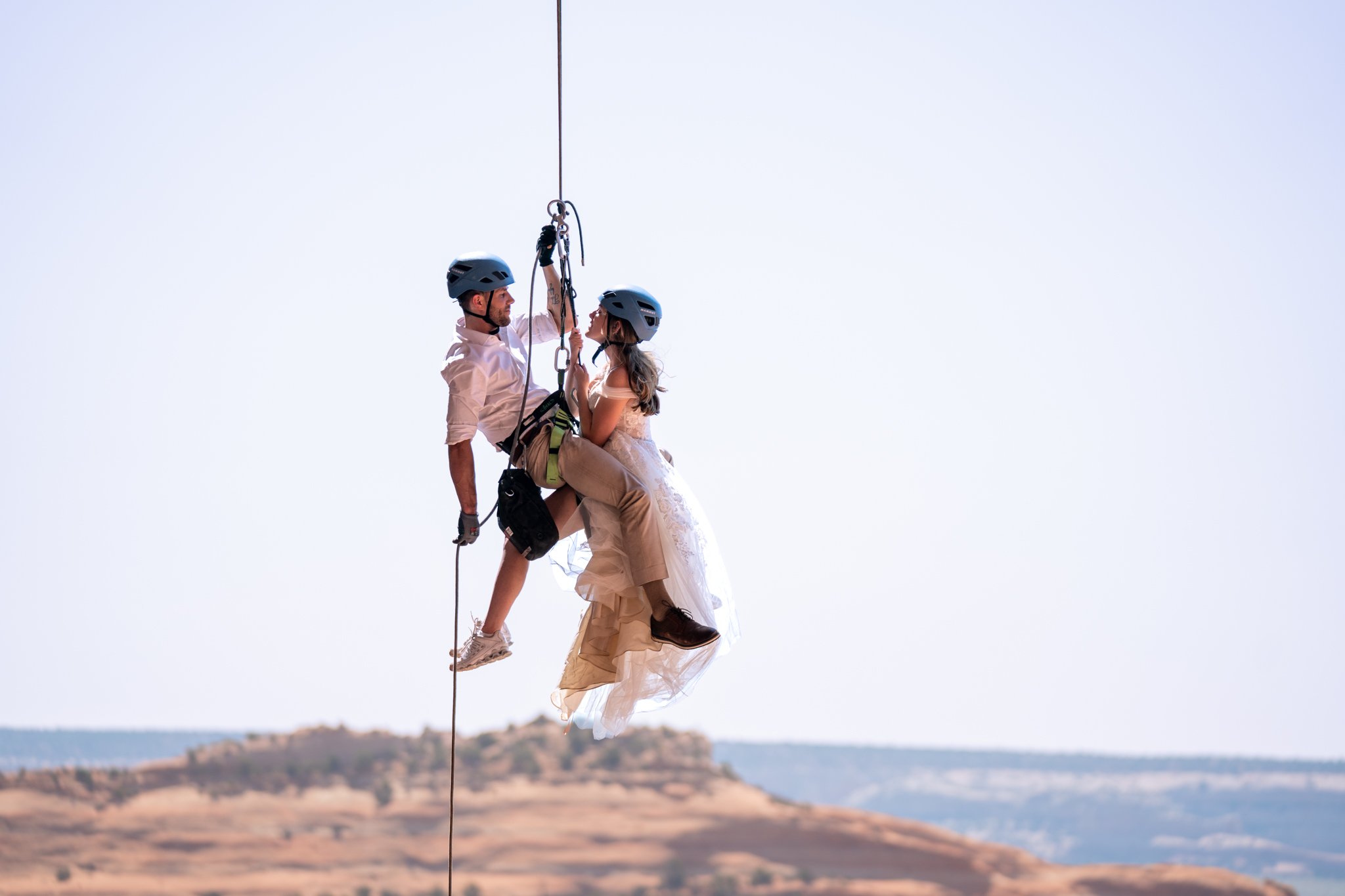 A bride and groom rappel down from a rock together in Moab.