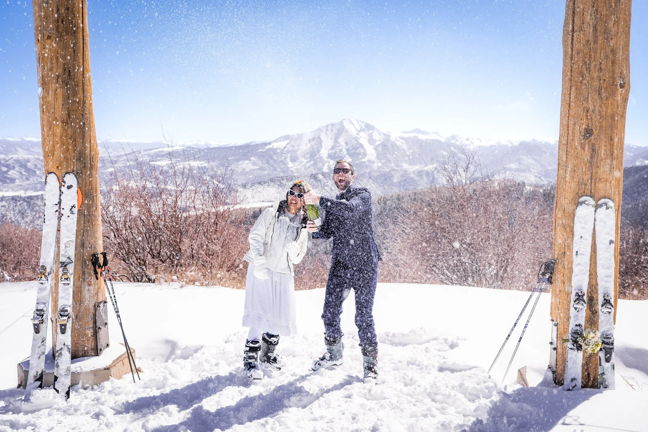 A bride and groom celebrate with champagne on a ski hill.
