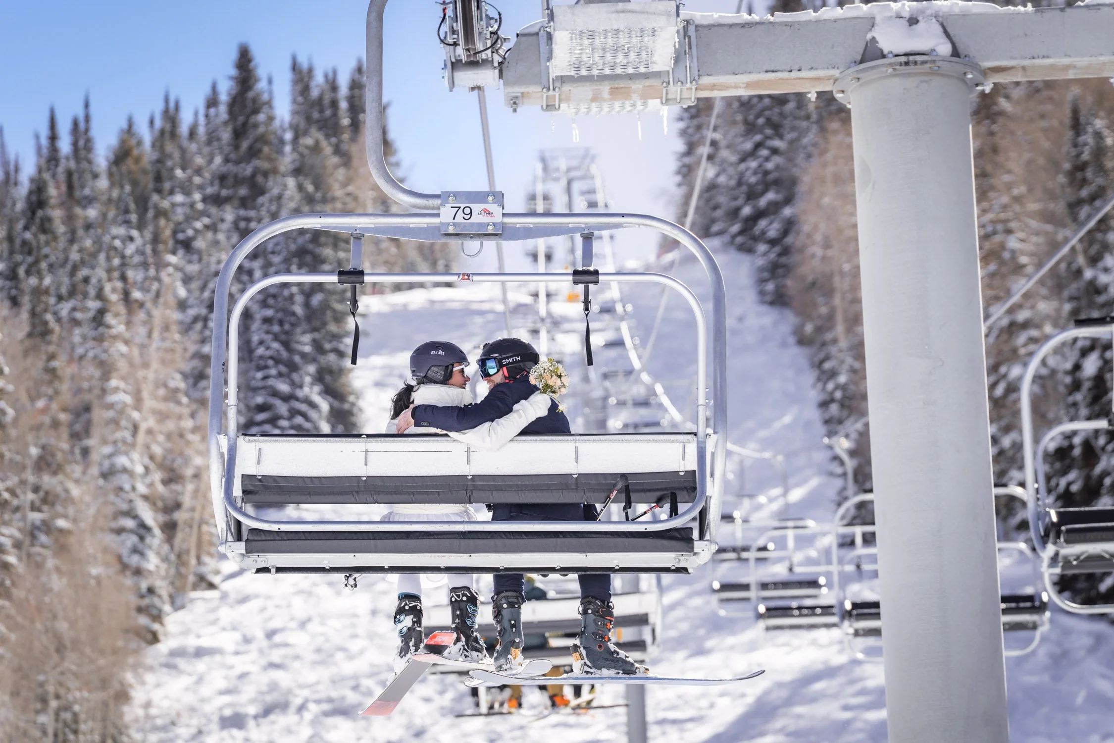 A bride and groom smile at each other on a ski lift.