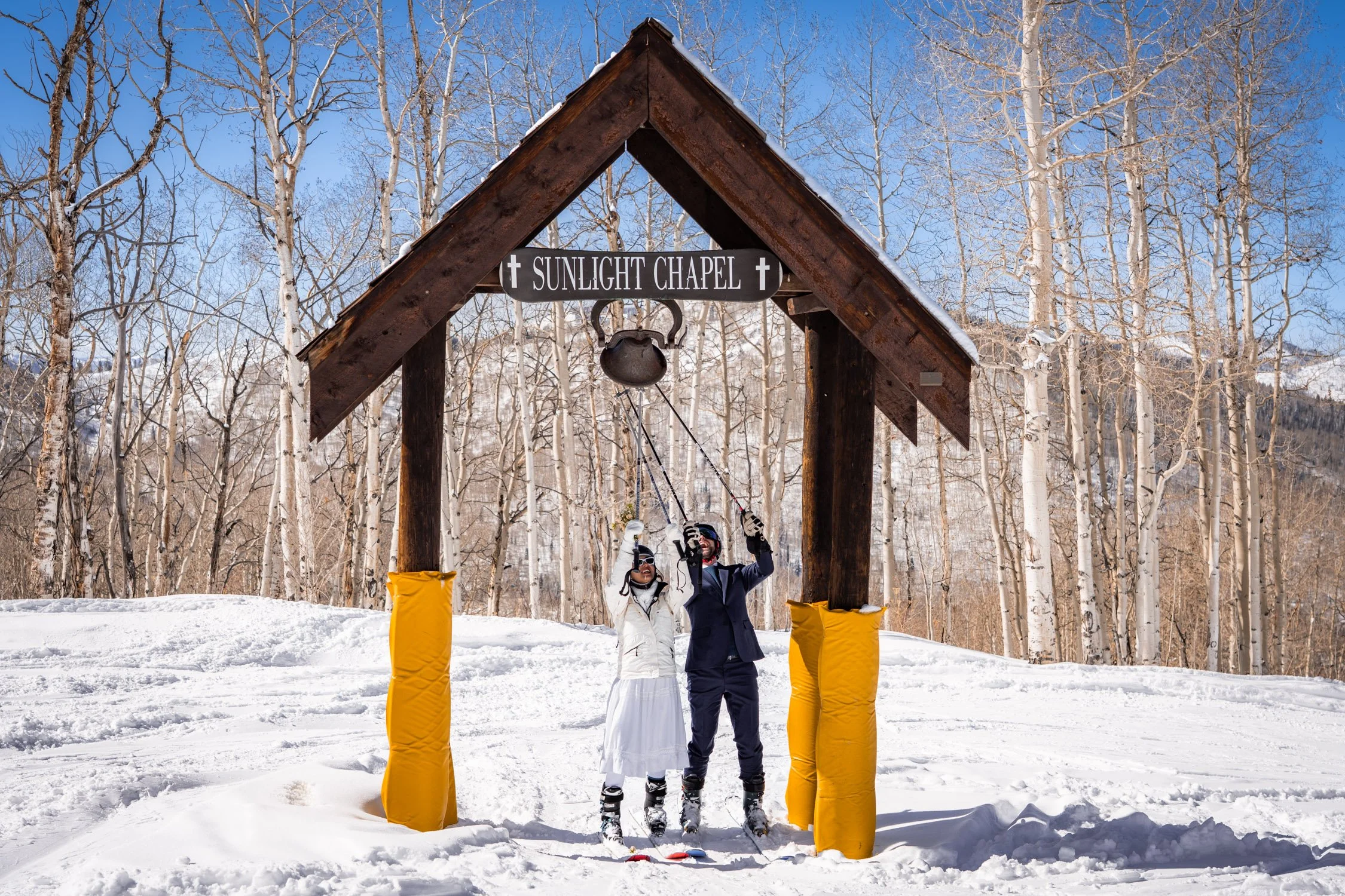 A bride and groom ring a bell in celebration on a ski resort in Colorado.