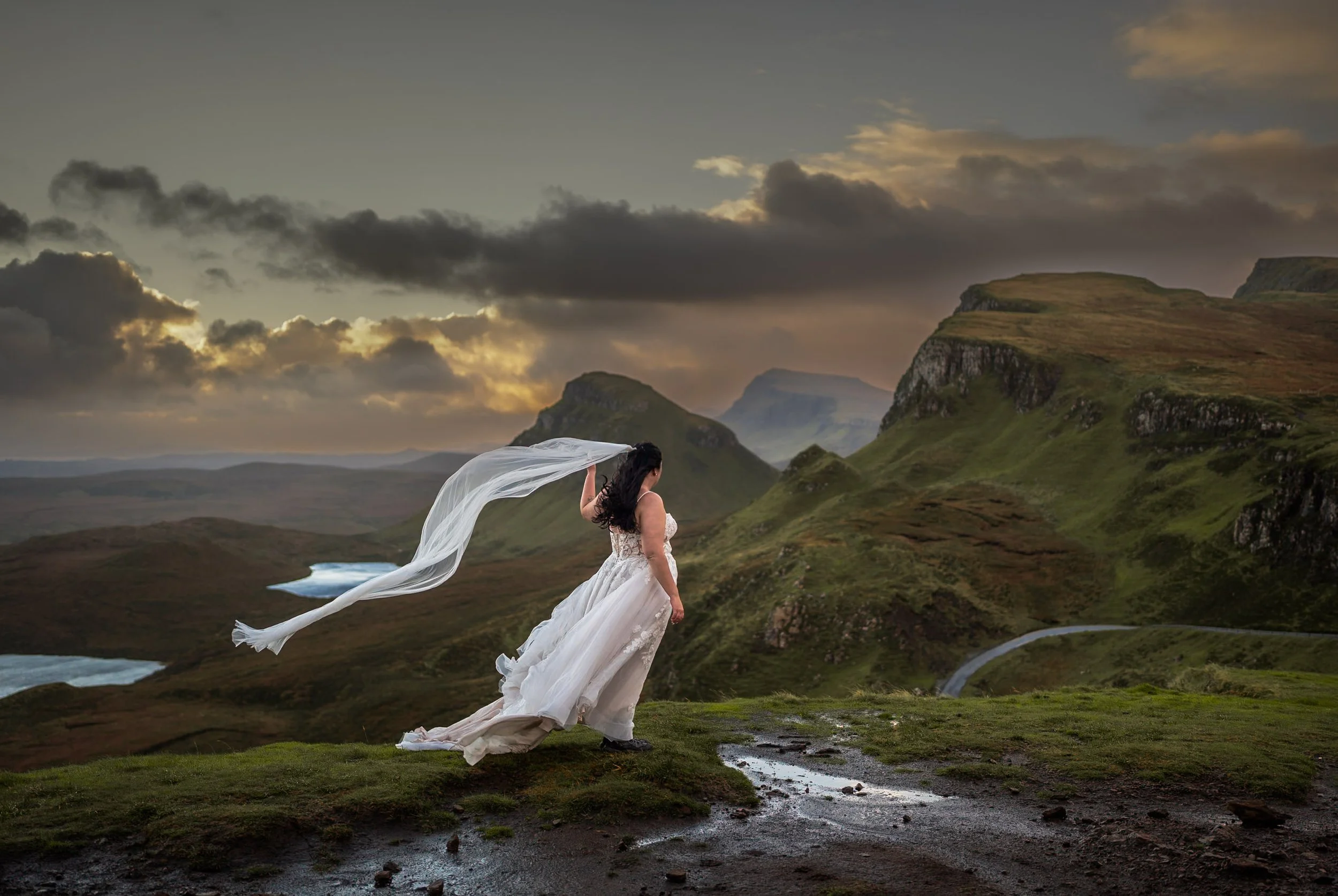 A bride stares at the grassy hills of Scotland while her veil blows in the wind.