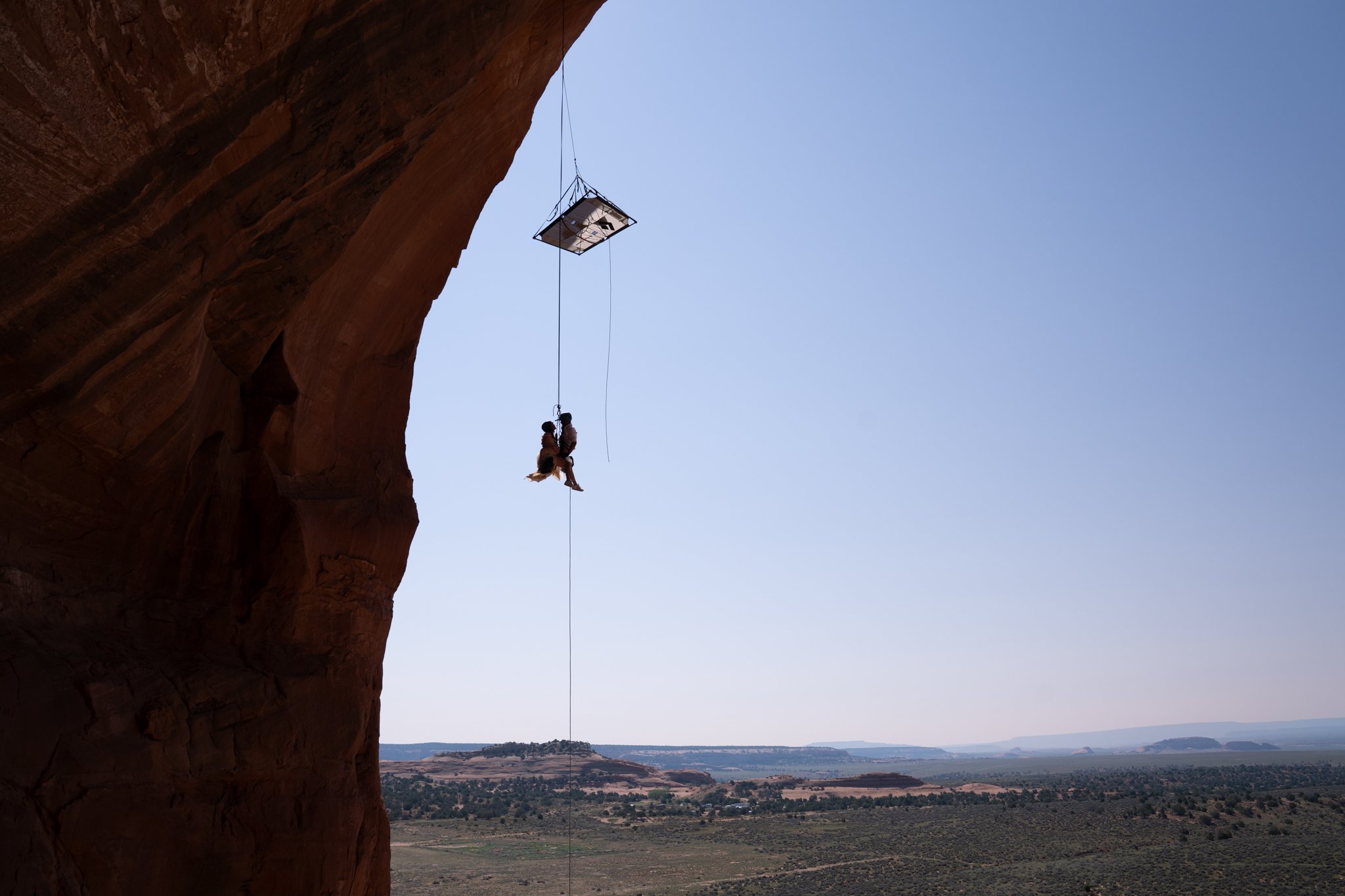 A silhouette of a bride and groom rappelling from a suspended portaledge after rock climbing in Moab.