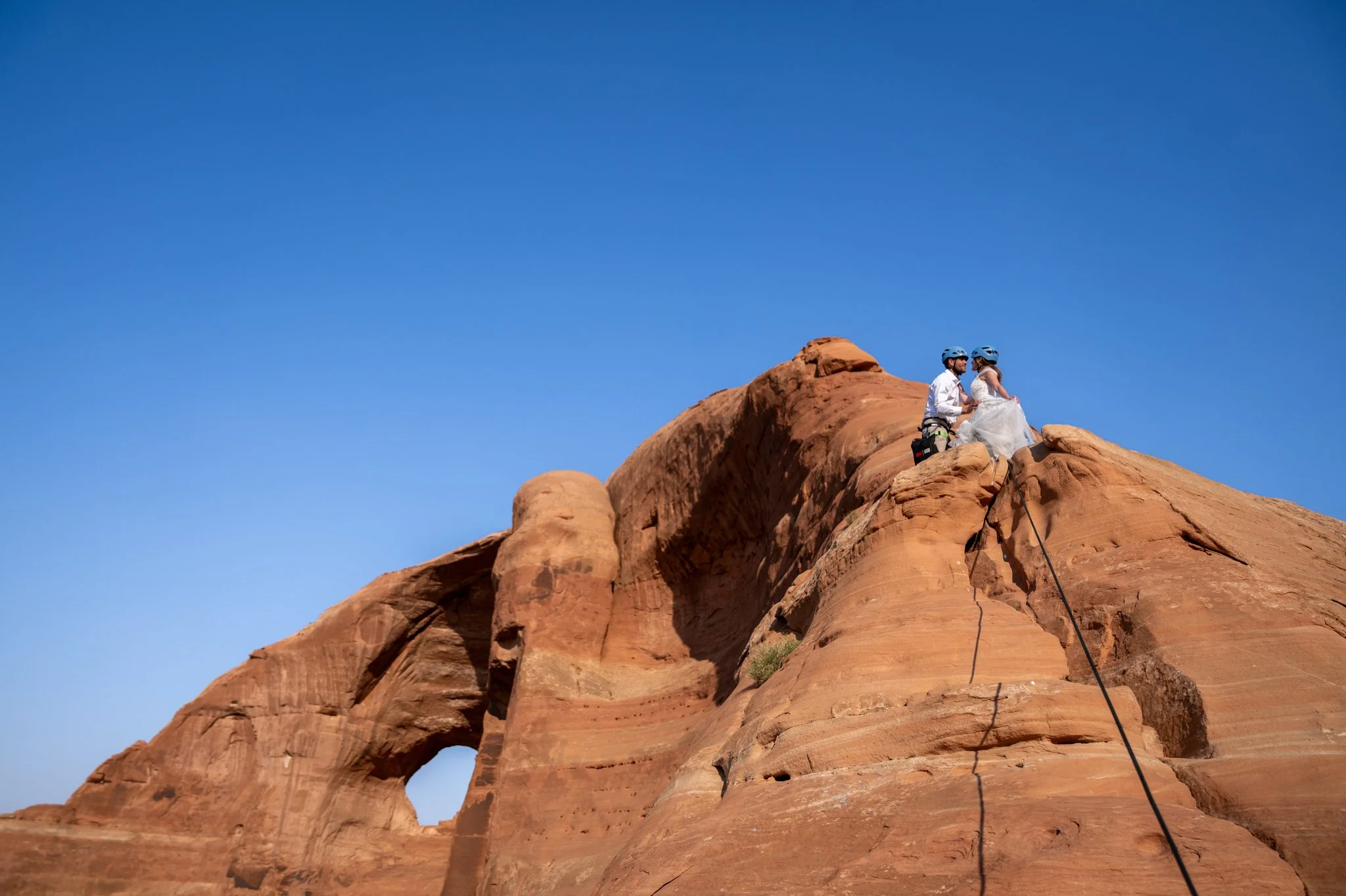 A bride and groom kiss on a red rock in Moab after climbing.
