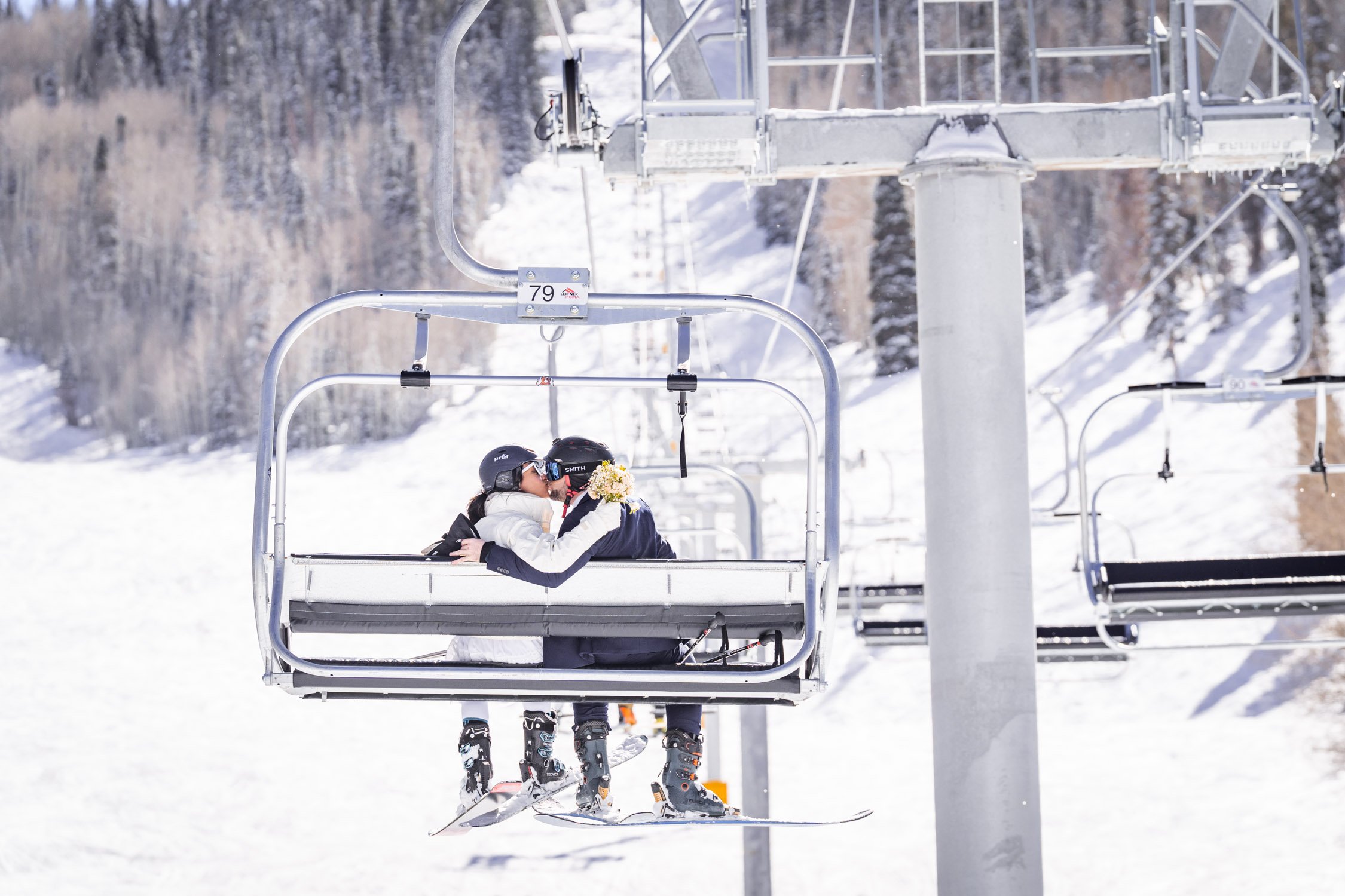 A bride and groom share a kiss on a chair lift on a ski resort in Colorado.