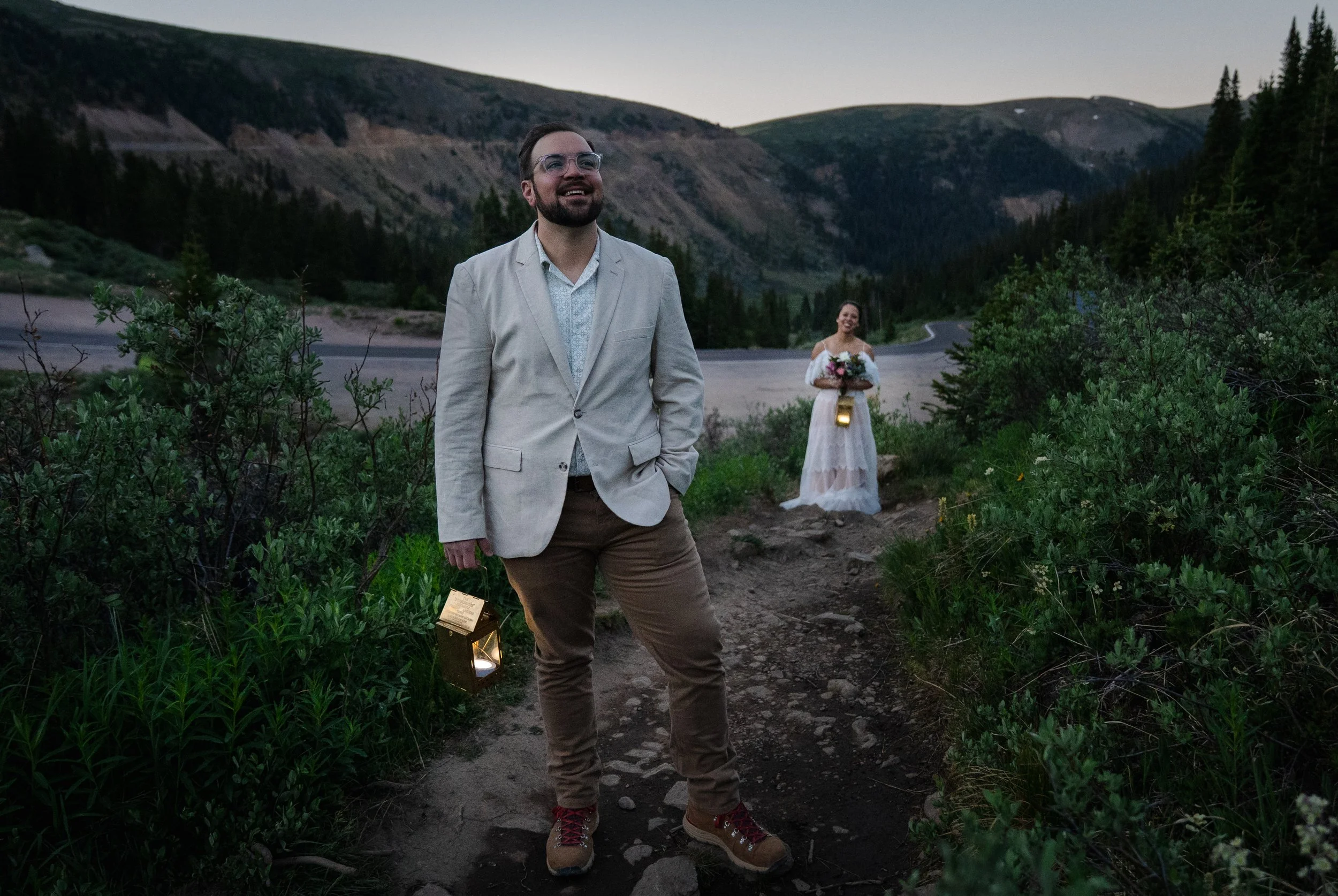 A groom waits expectantly with a lantern in the pre-dawn light as his bride approaches for a first look for a Colorado elopement.