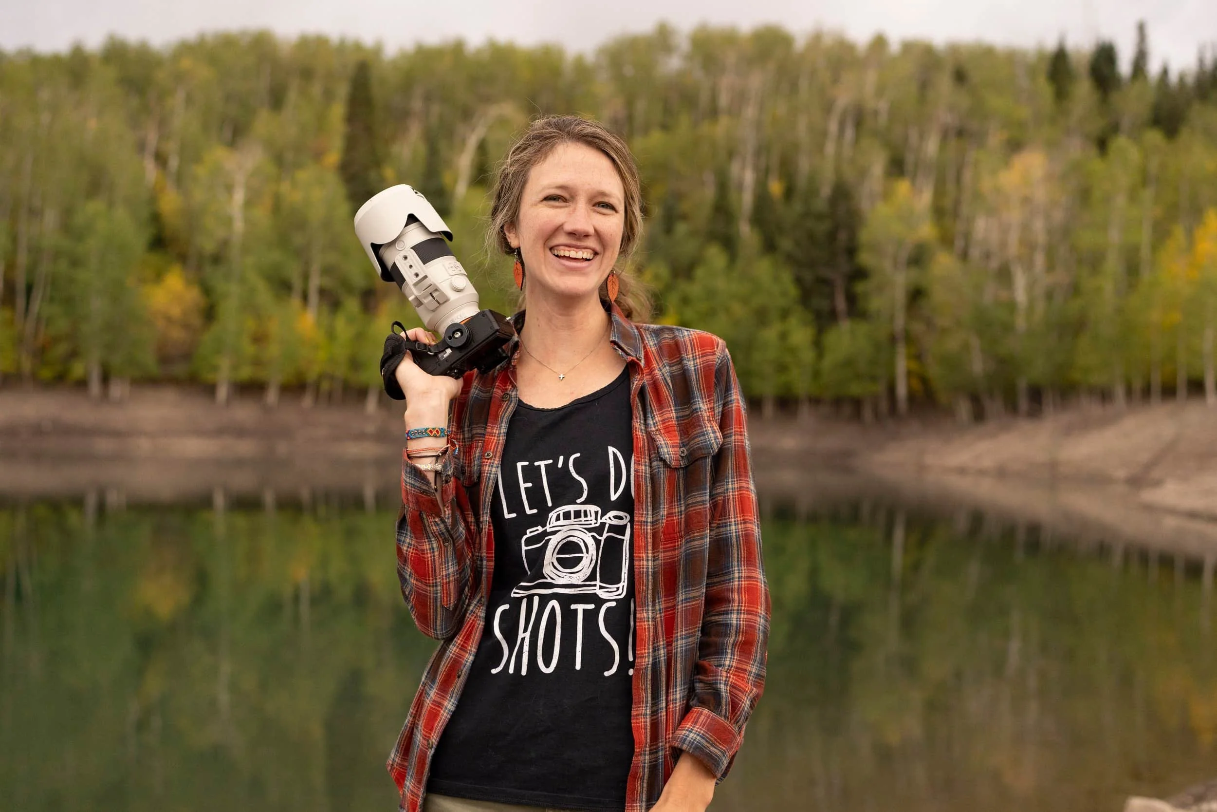 A girl smiles while holding a camera in front of a Colorado lake