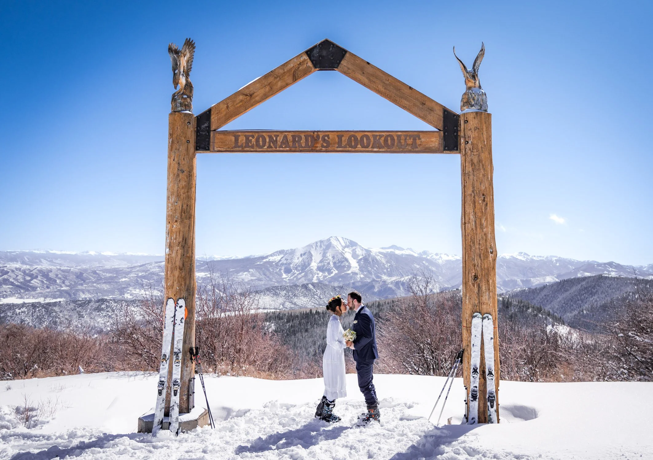 A bride and groom kiss on a snowy lookout on a ski resort in Colorado.