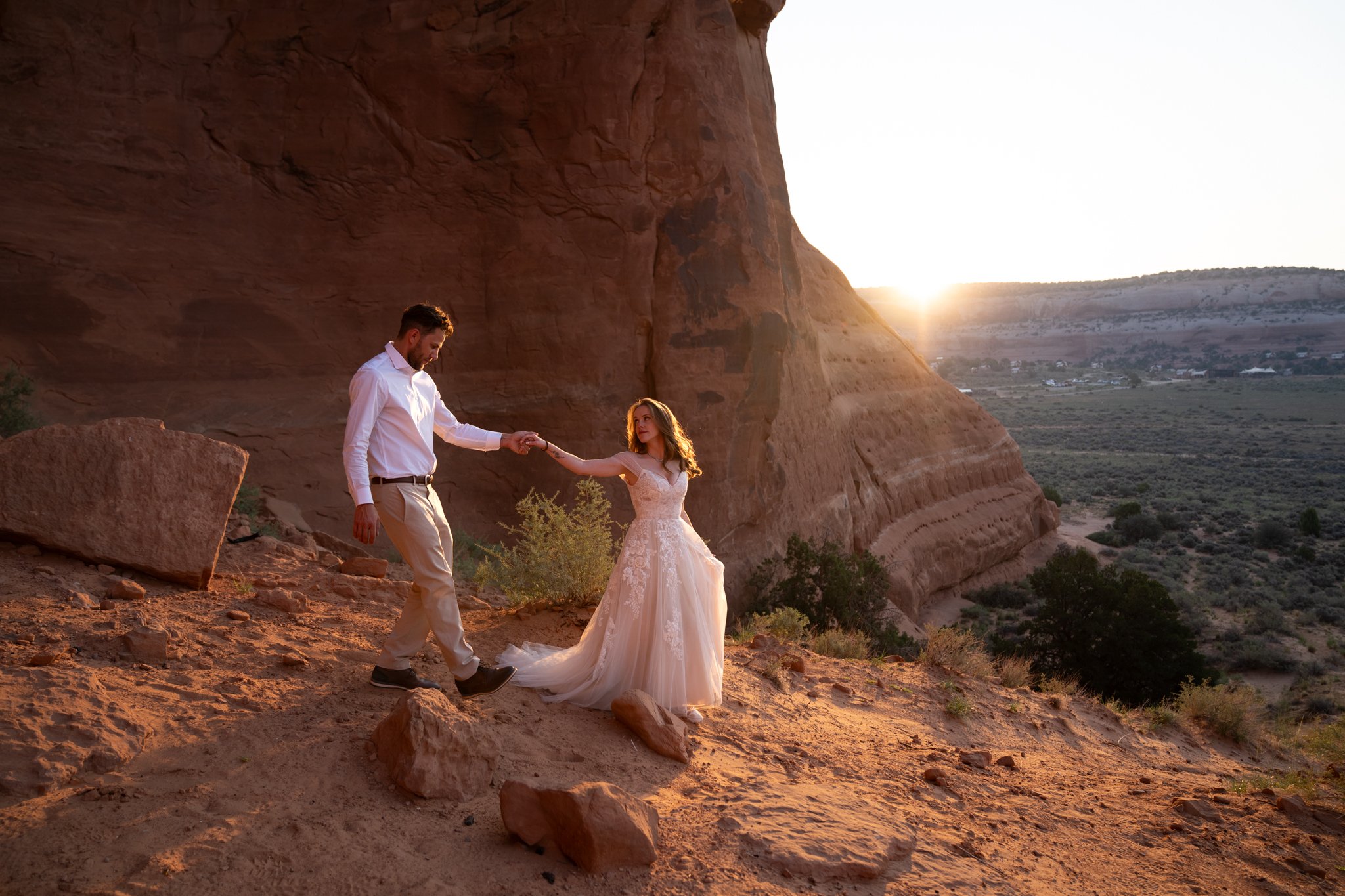 A bride leads a groom down a desert path at sunrise in Moab.