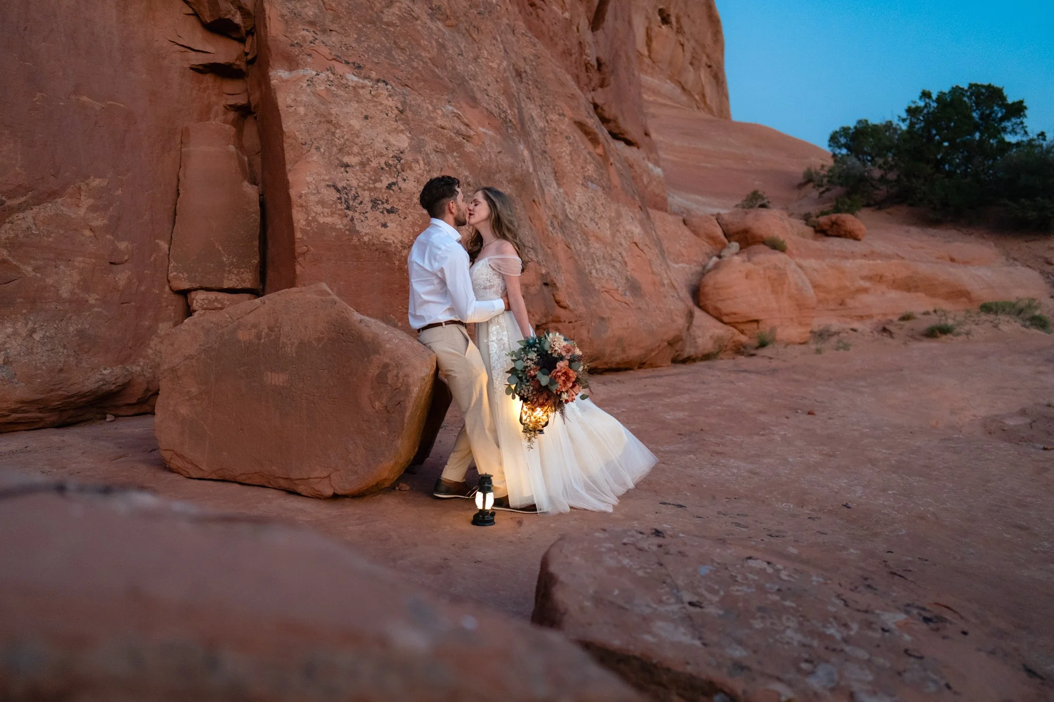 A bride and groom kiss in front of red rocks in Moab, Utah.