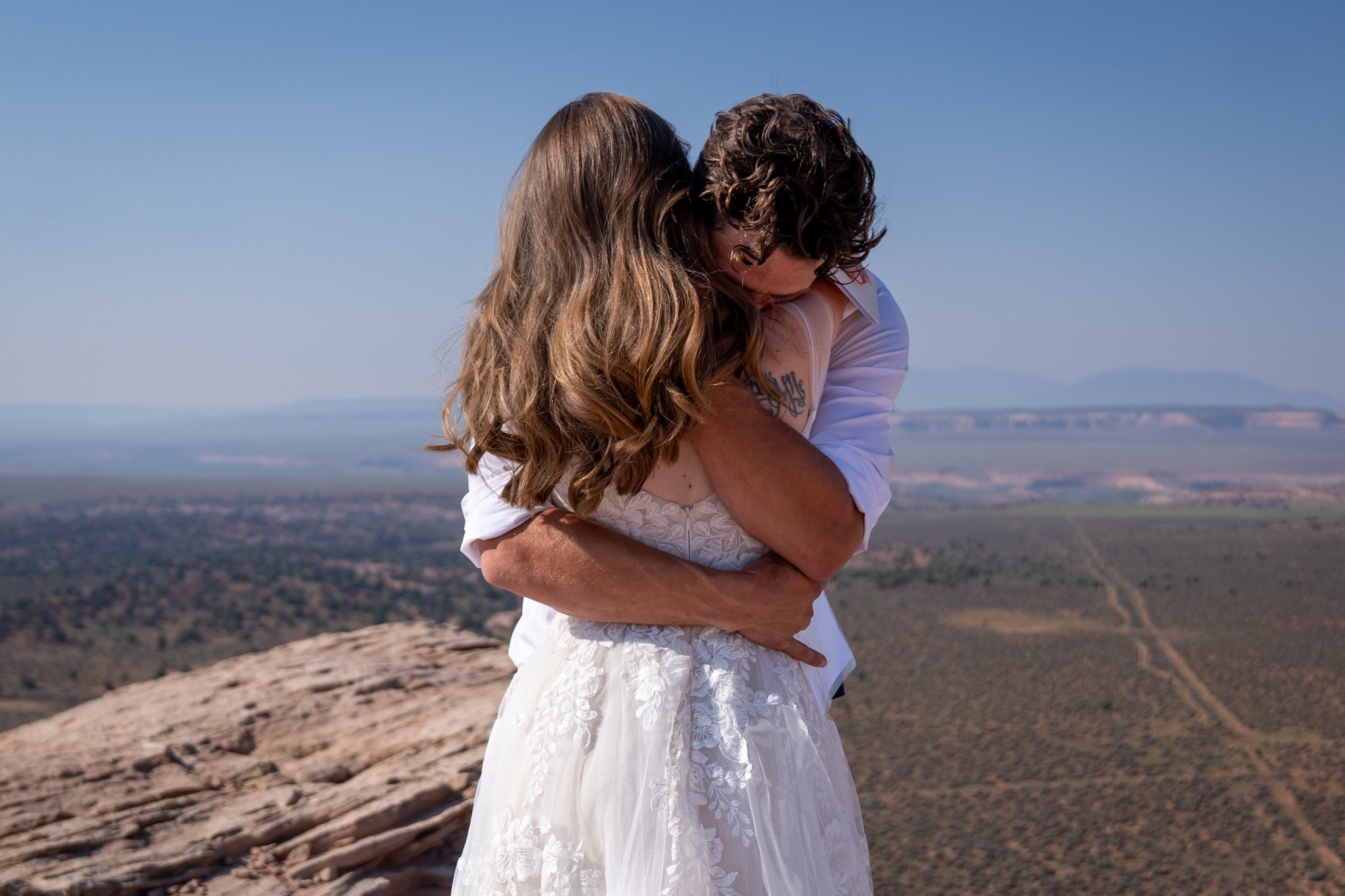 A bride and groom hug emotionally on top of a rock after saying vows.