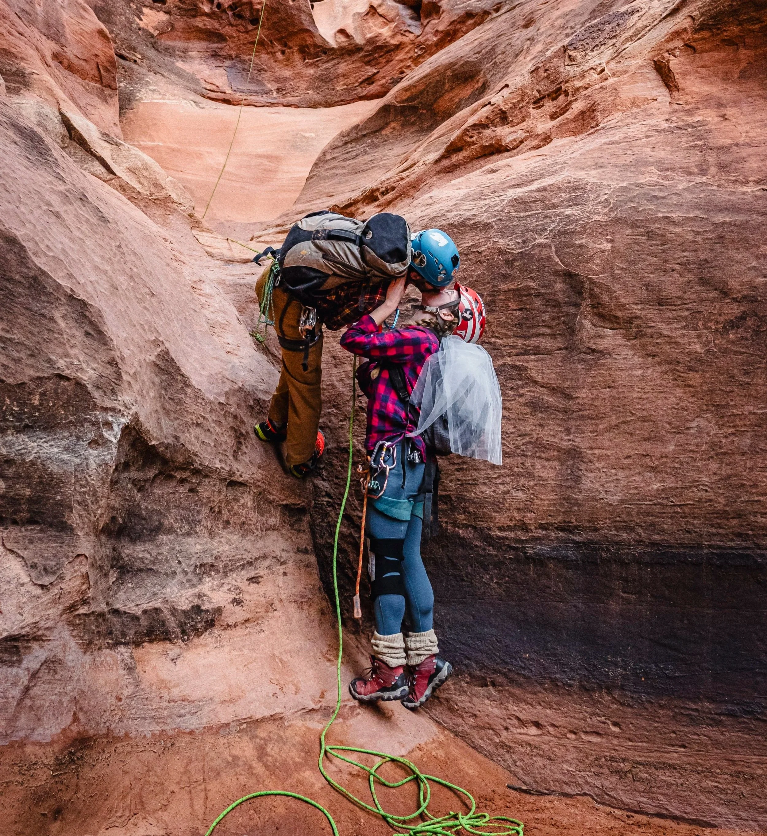 A bride and groom rappel through a canyon and stop to kiss.