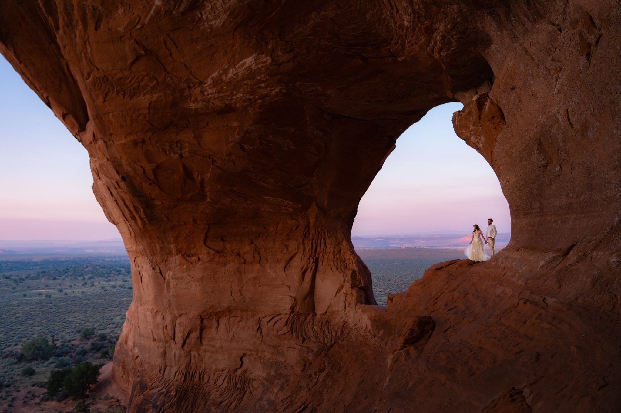 A bride and groom look into the distance as they stand in a red rock archway in Moab.