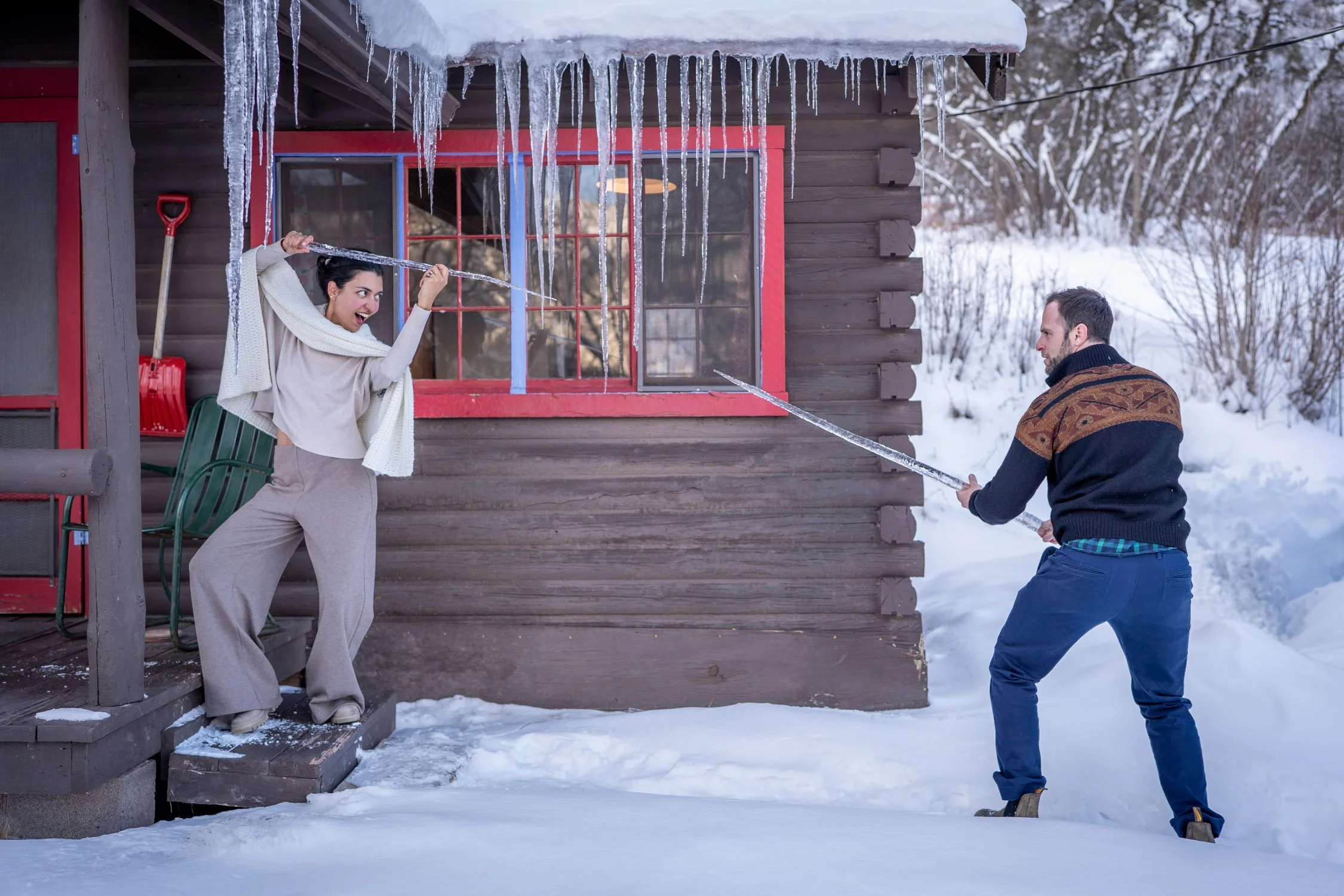 A bride and groom pretend to sword-fight with icicles outside of their Colorado cabin.