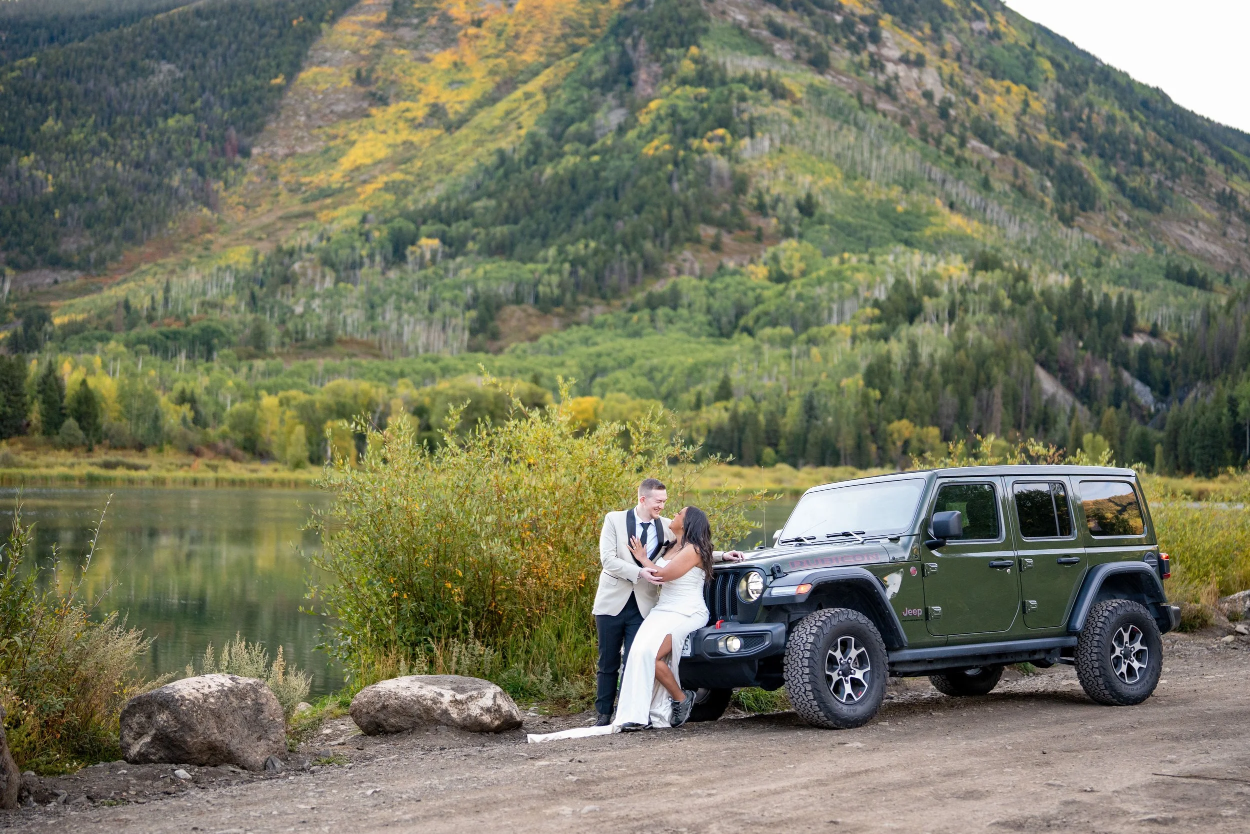 A bride leans against a green Jeep as her groom stands near her in front of a mountain in Marble, Colorado.