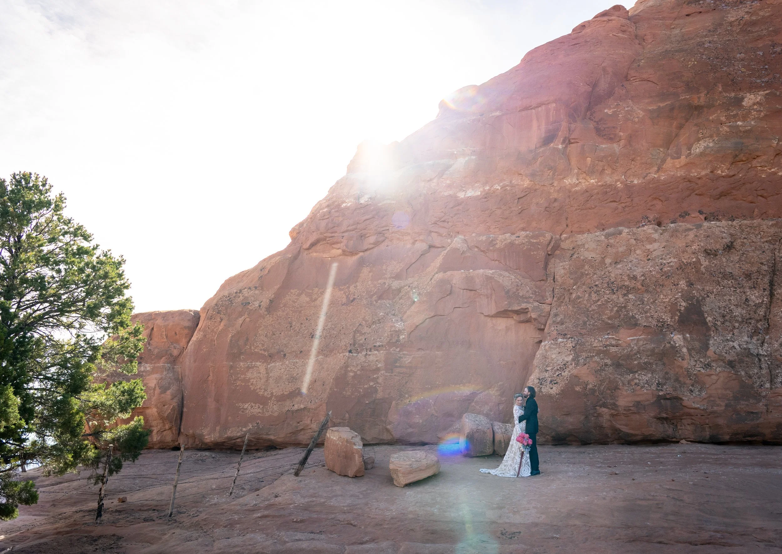 A bride and groom hold each other by a red rock at sunrise in Utah.