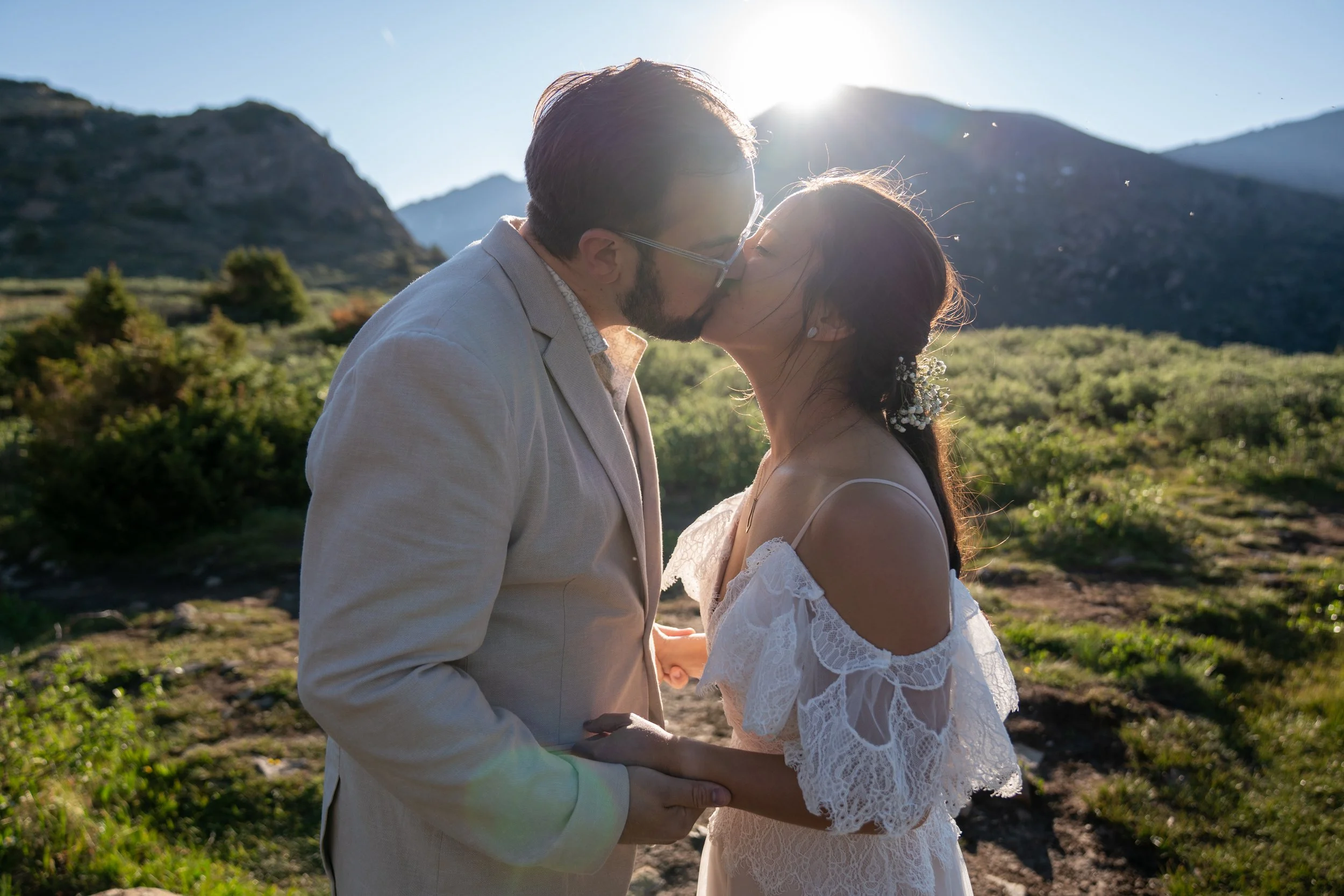 A bride and groom kiss as the rising sun crests a mountain peak behind them.