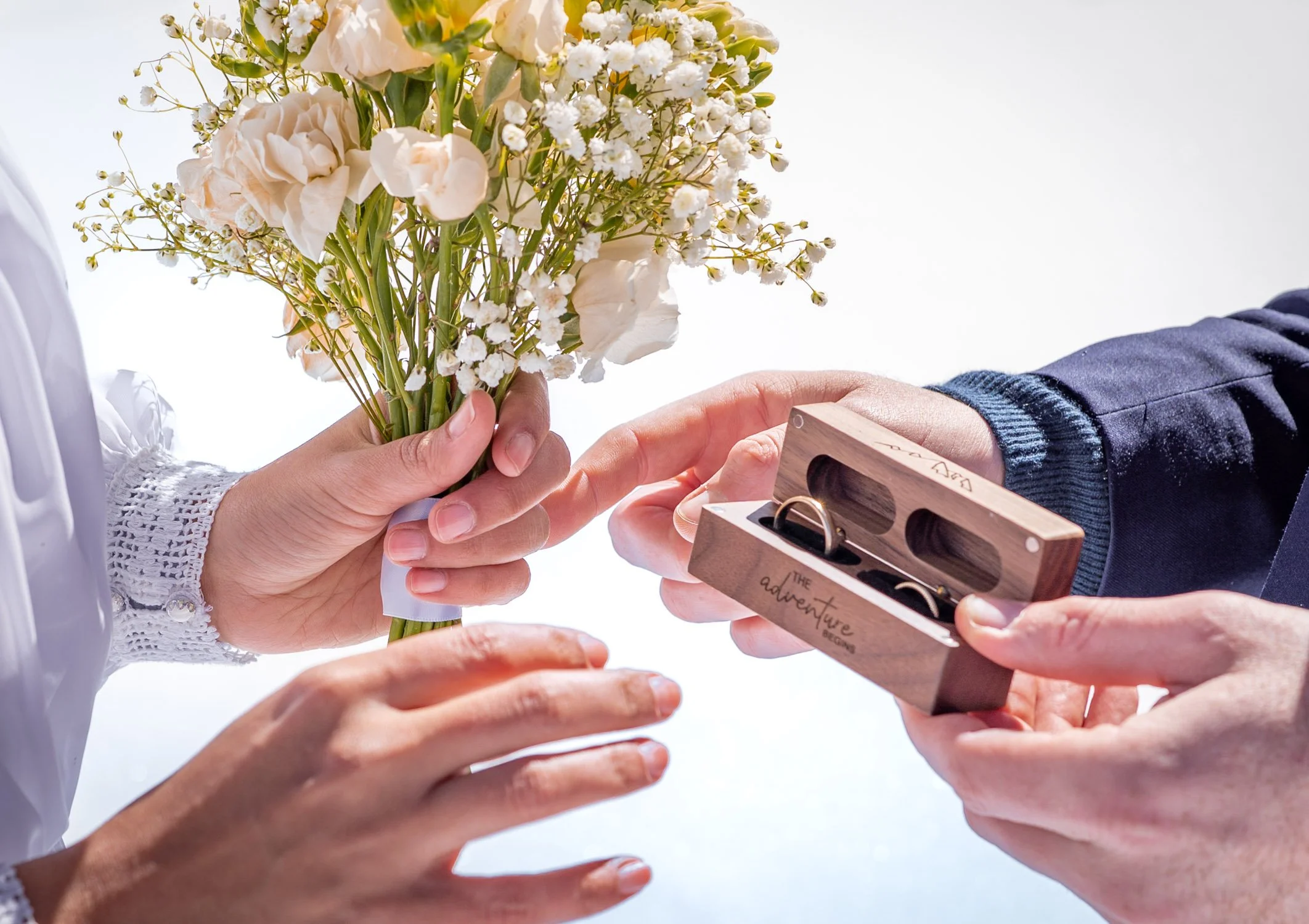 A bride and groom hold rings and flowers on top of a ski resort in Colorado.