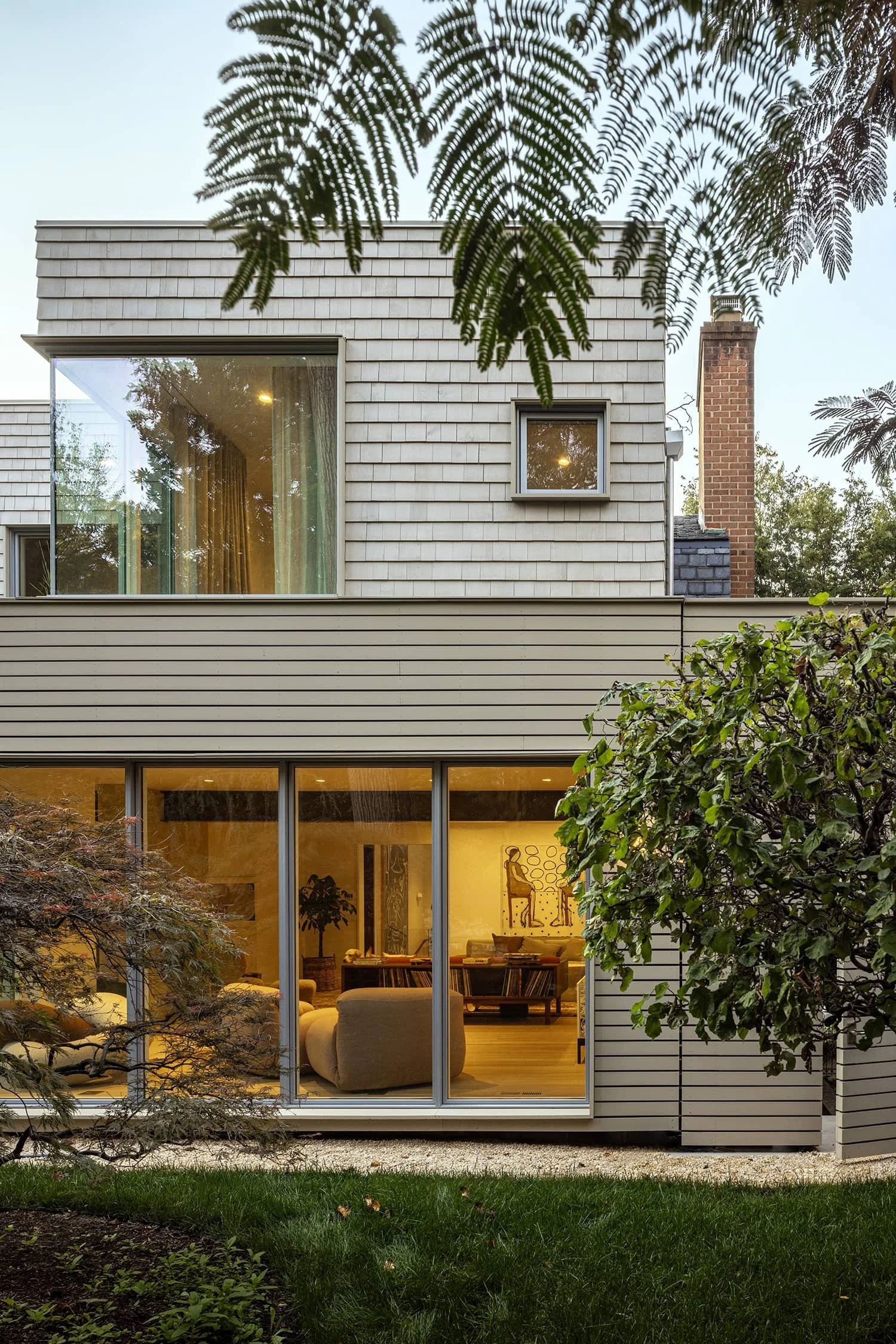 Modern home exterior with glass walls and contemporary siding nestled among trees, designed by Fowlkes Studio in Kalorama, Washington, DC.