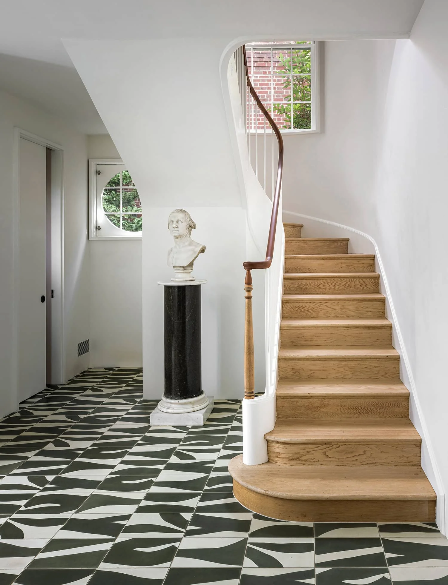 Sweeping staircase in modern entryway with cement tiles, historic bust and stripped wooden staircase in Washington, DC
