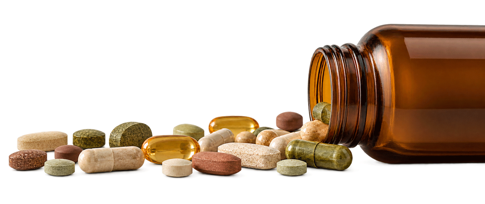 Supplement capsules and tablets spilling from an amber glass bottle.