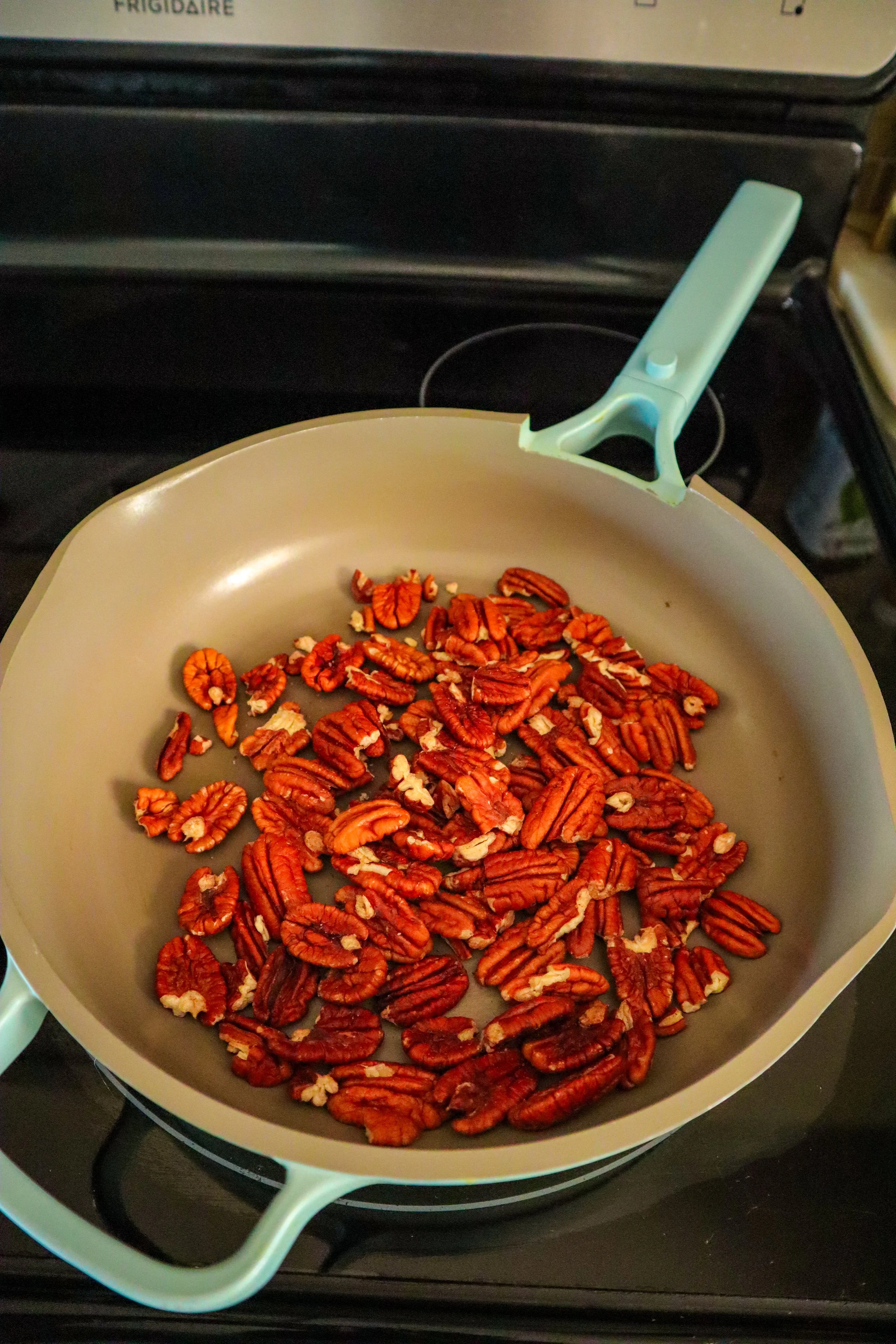  Raw pecan halves toasting in a nonstick pan over medium heat for the spiced praline pecans recipe. 