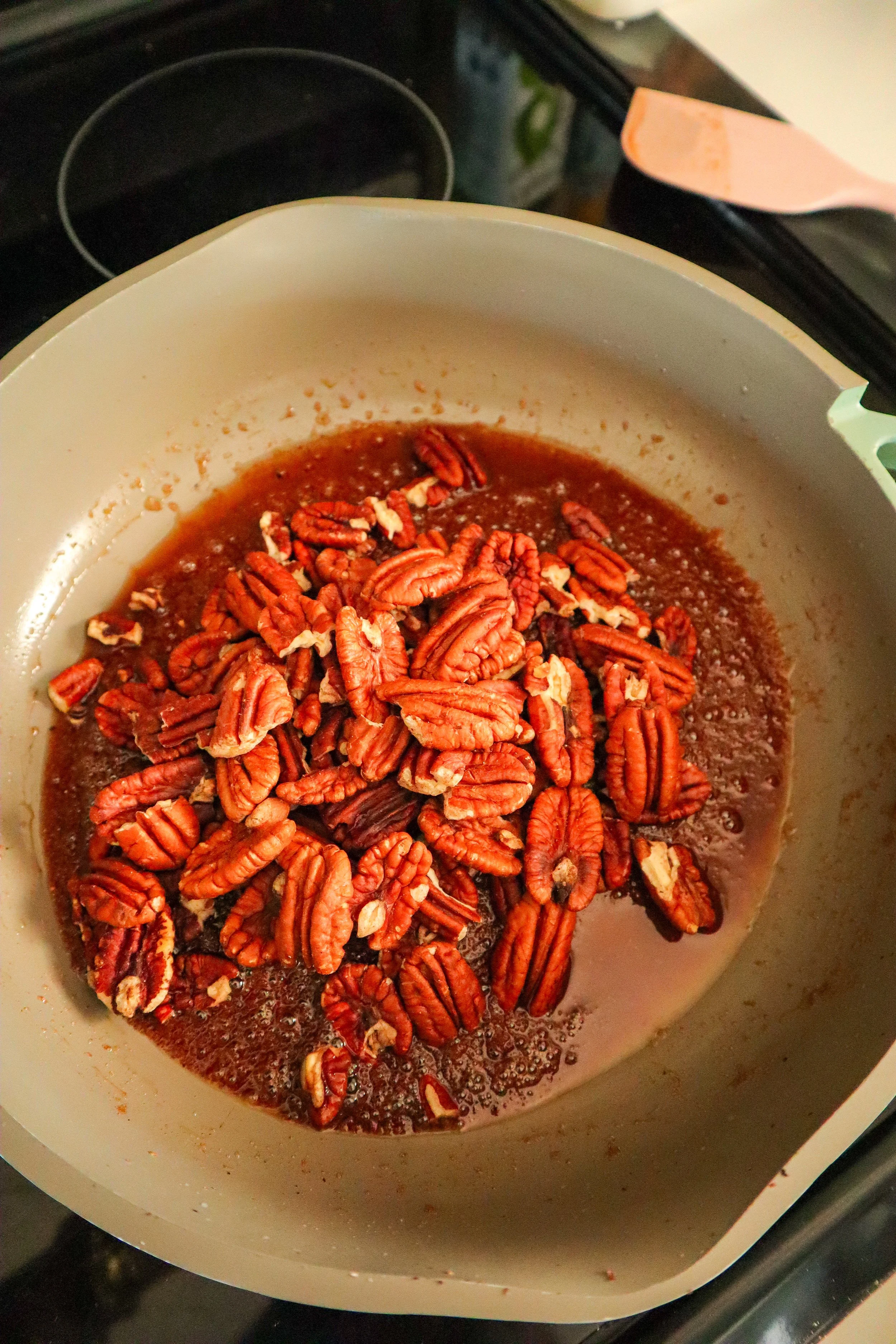 Toasted pecans added to the sugar mixture in a pan to make candied pecans. 