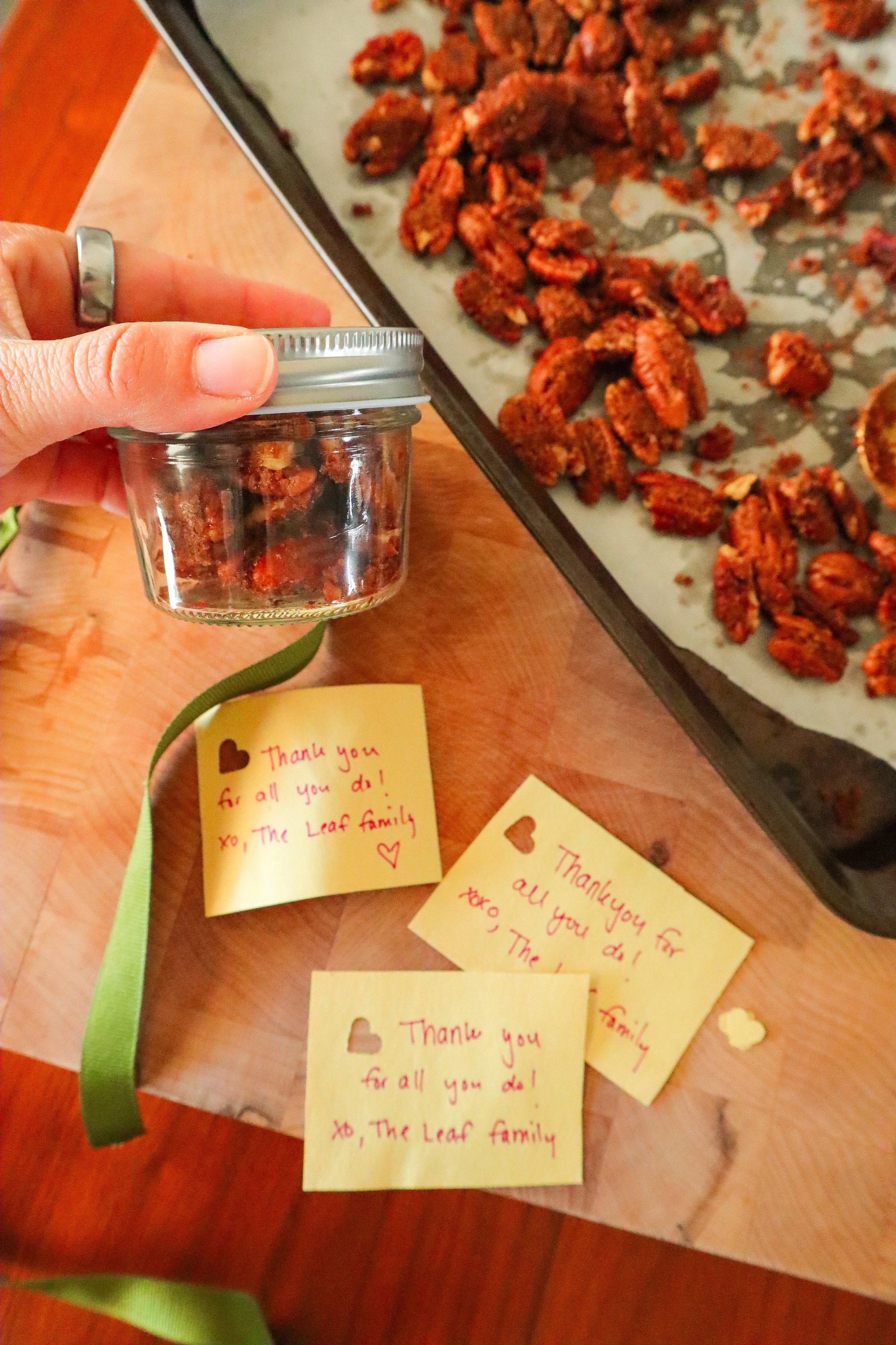  Hand holding a small mason jar filled with spiced praline pecans, ready for gifting. 