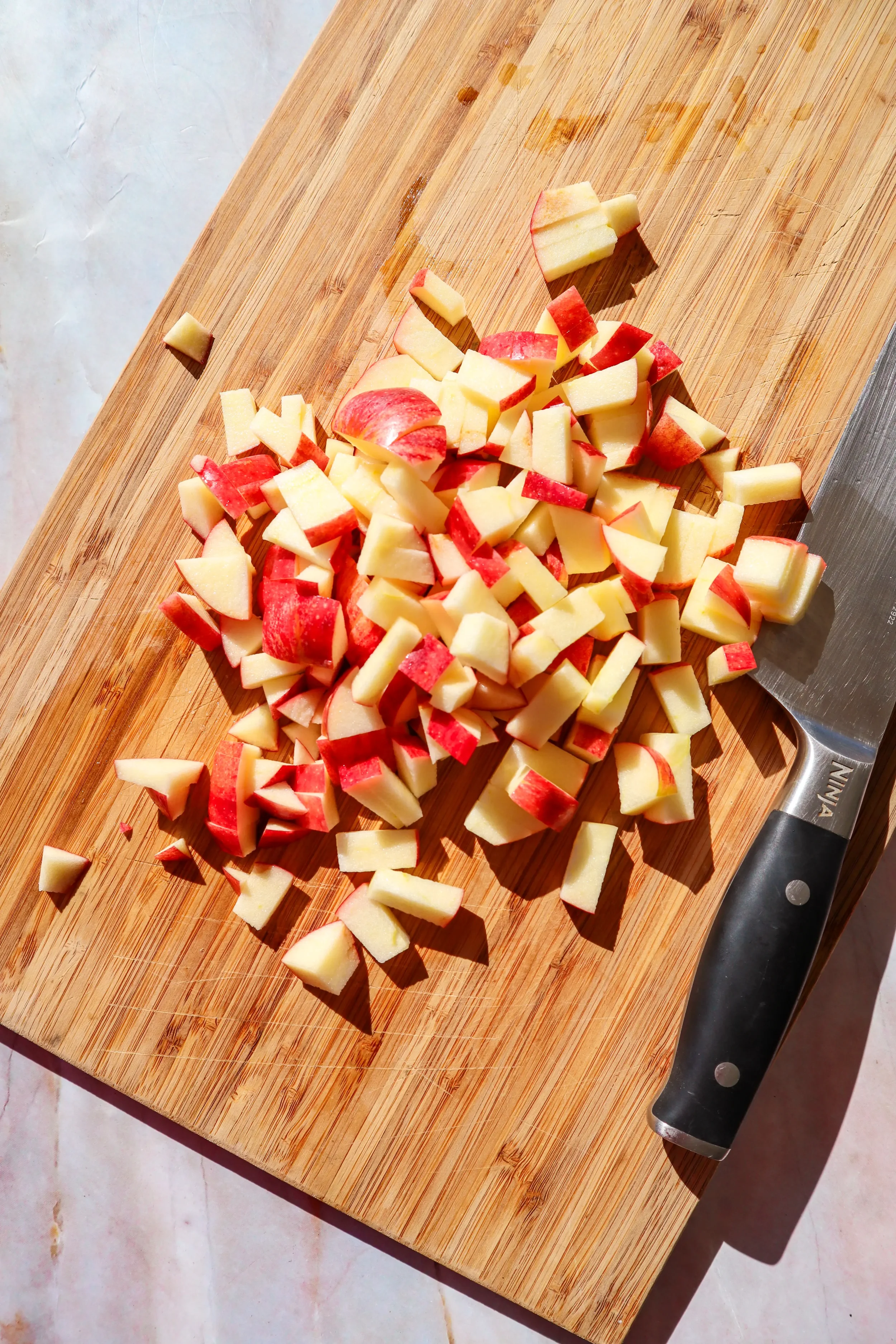  Diced apples on a cutting board with a knife, ready for air fryer apples. 