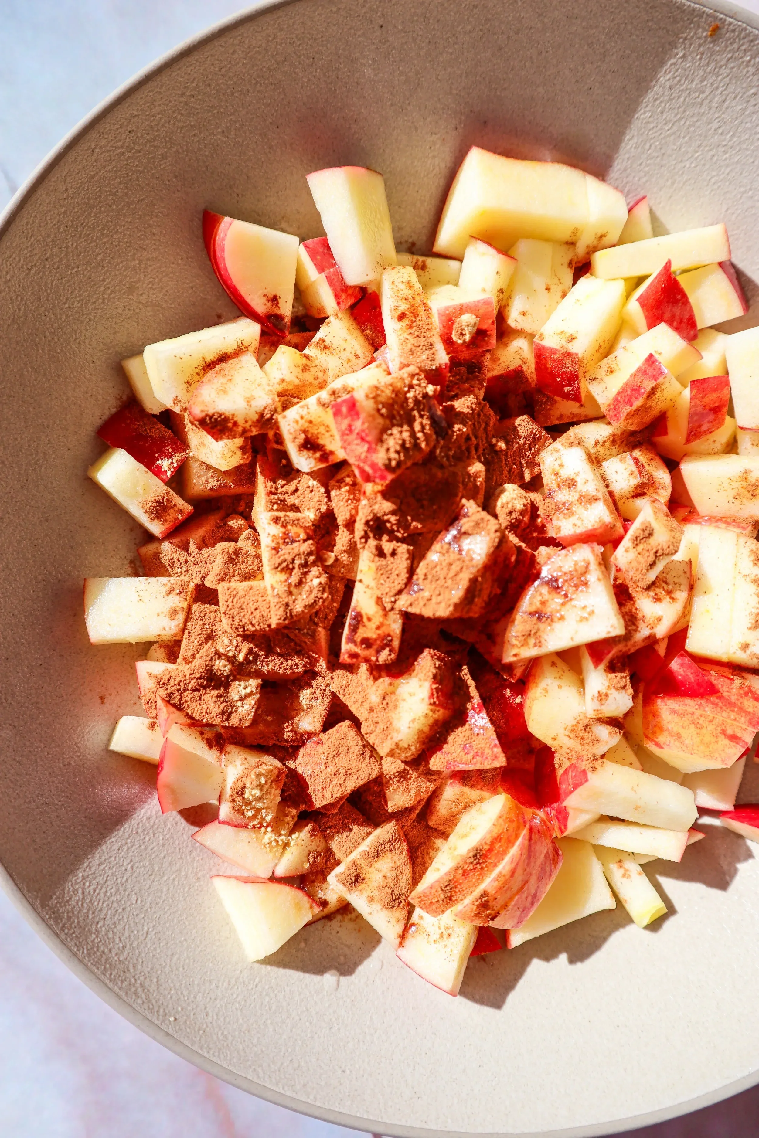  Diced apples in a bowl topped with cinnamon and spices, ready for air fryer apples. 