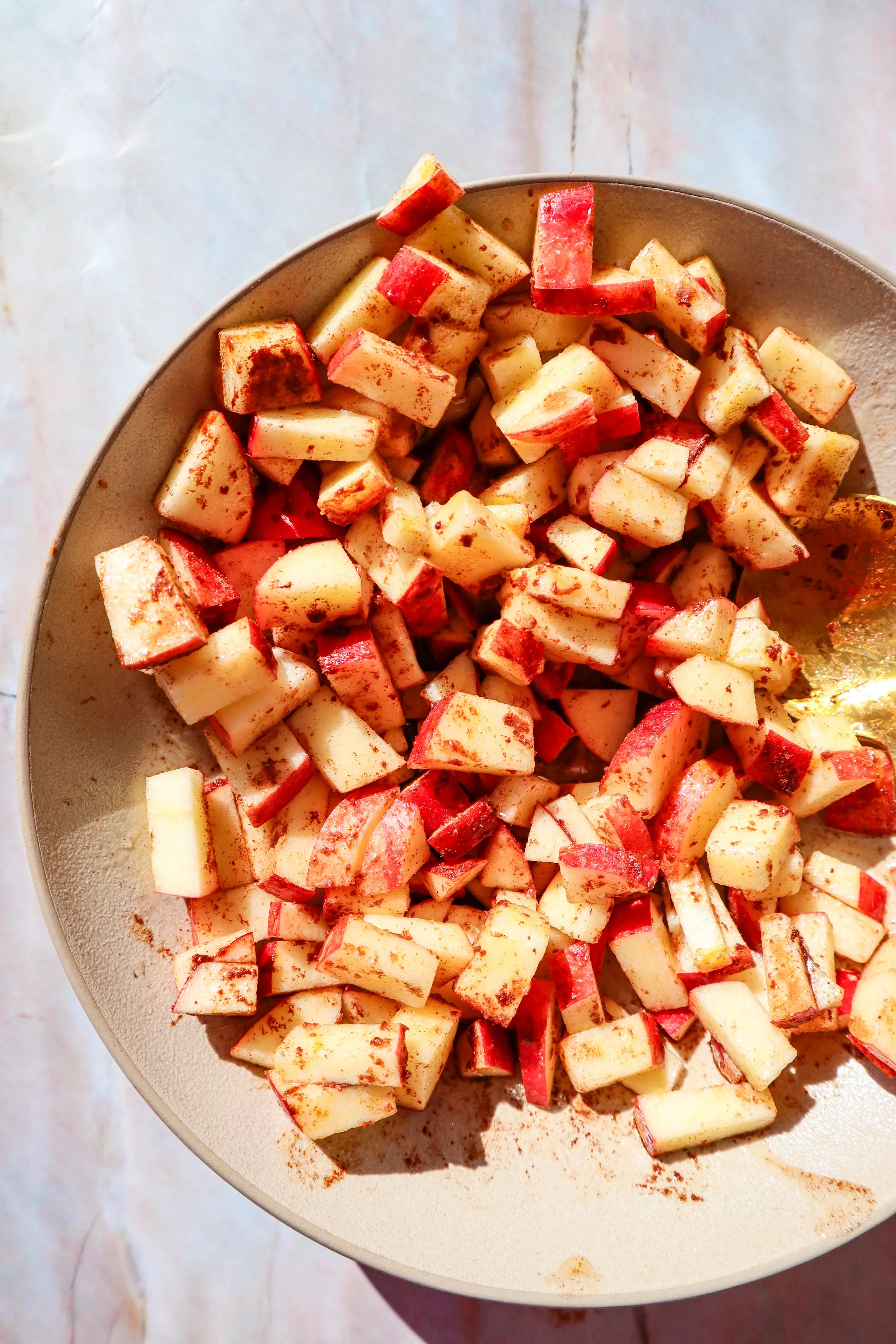  Apples evenly coated with cinnamon and spices in a bowl for air fryer apples. 