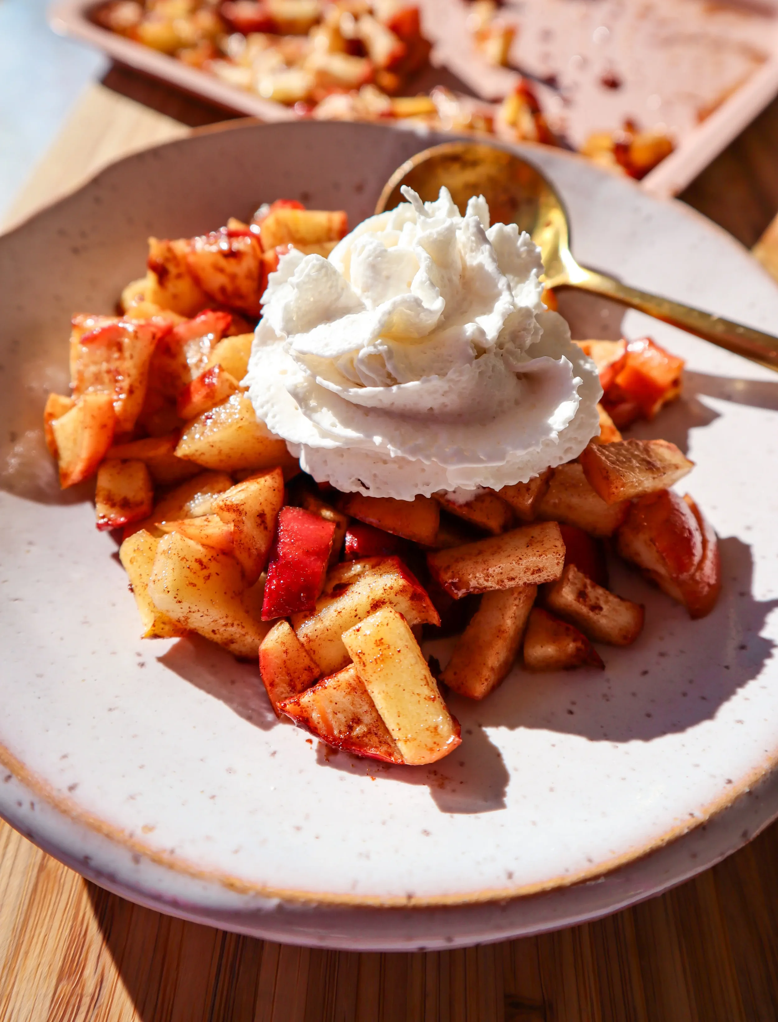 Air fryer apples with cinnamon topped with whipped cream on a plate.