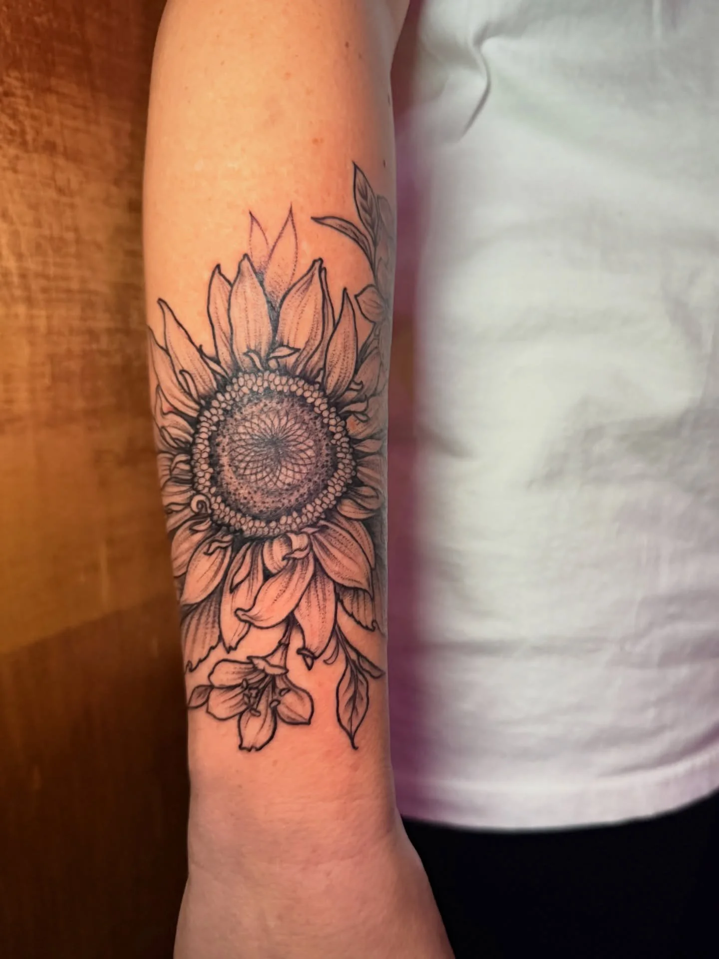 Sunflowers are so pretty! Working on this sleeve with a blacked out background in near the wrist faded into a light background at the top of the arm to accommodate an existing tattoo. For that reason there&rsquo;s very little shading off of the exter