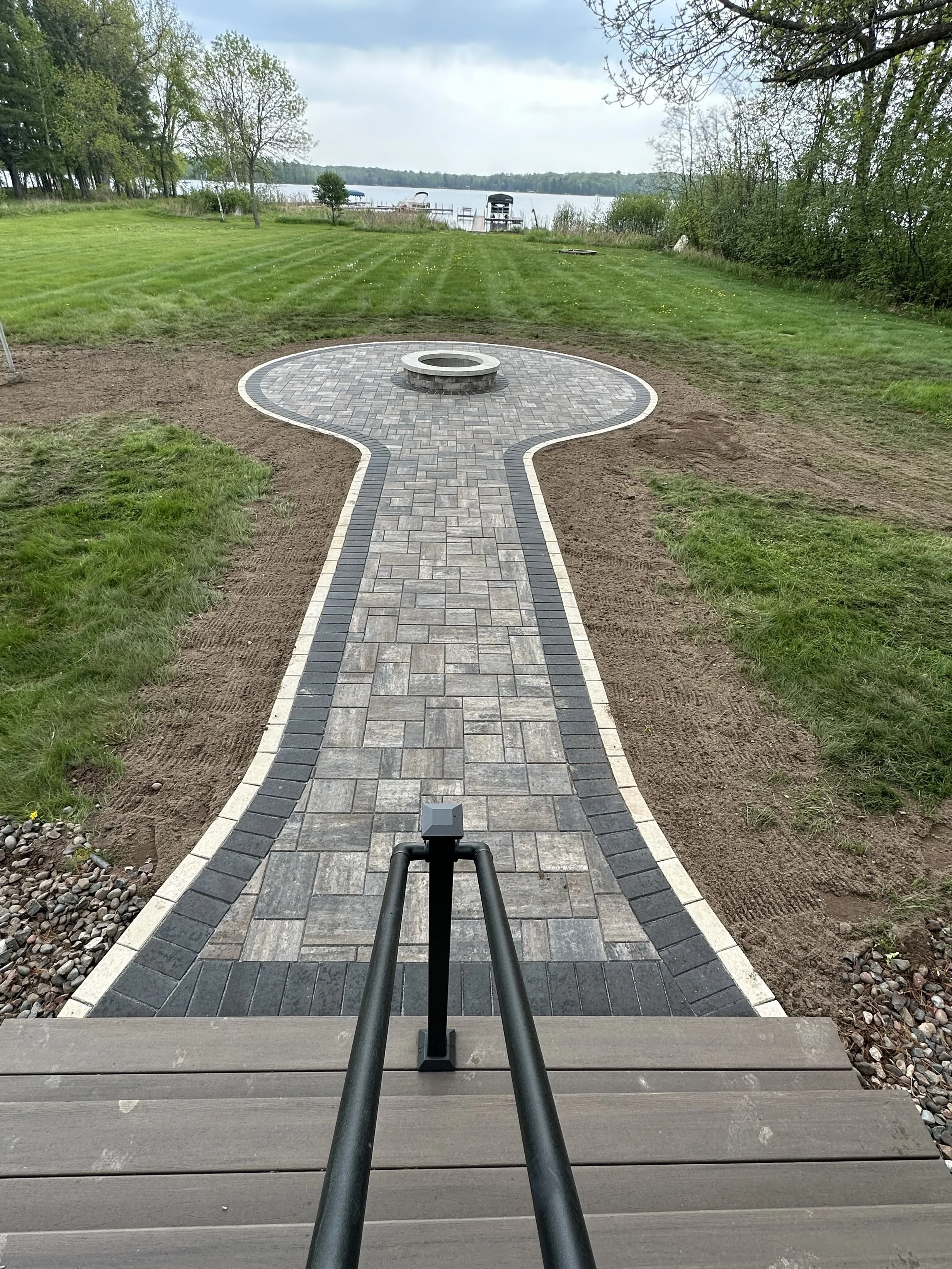 MB Landscapes newly paved walkway leading to a fire pit by a lake.