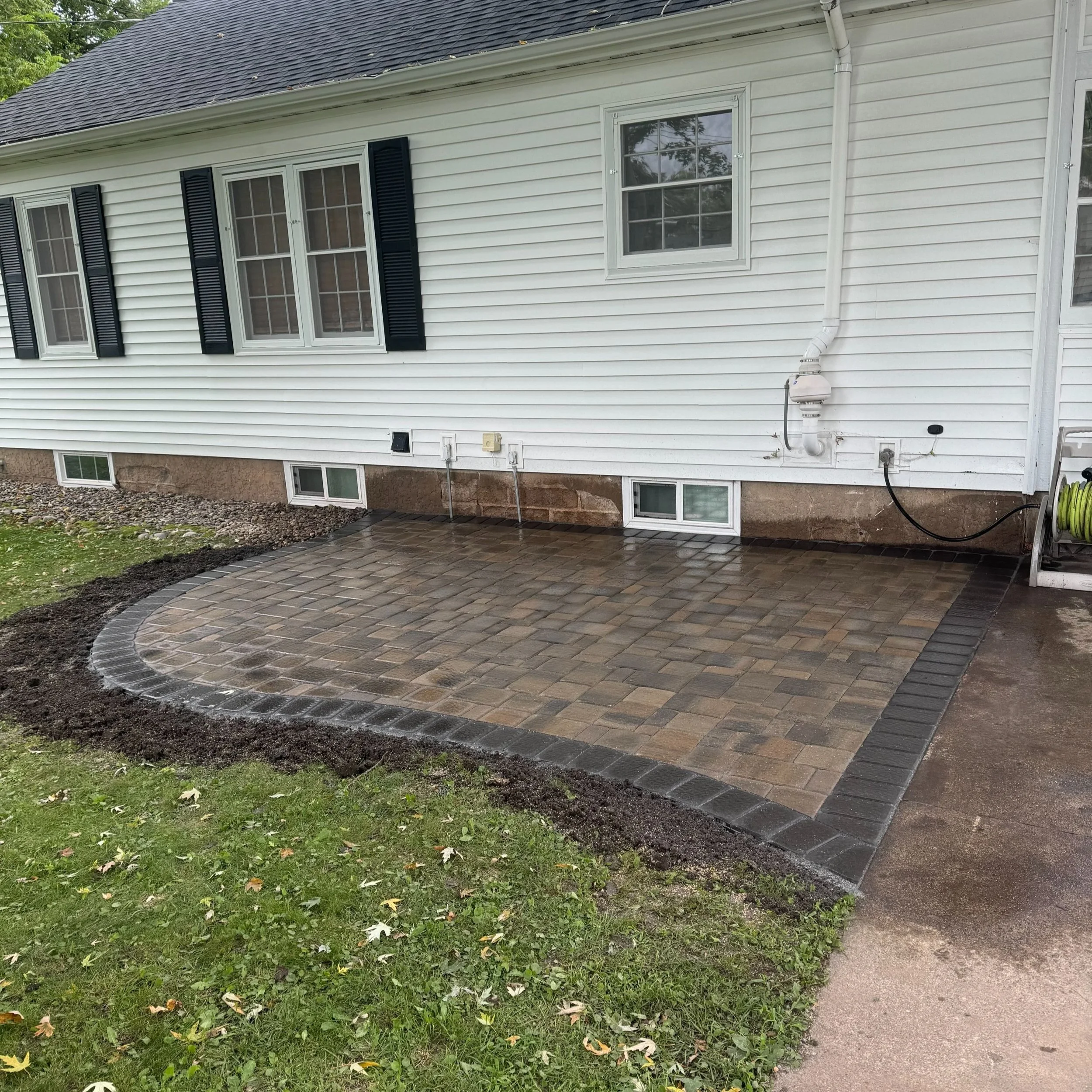 MB Landscapes installed newly paved backyard patio with brick and stone edging.