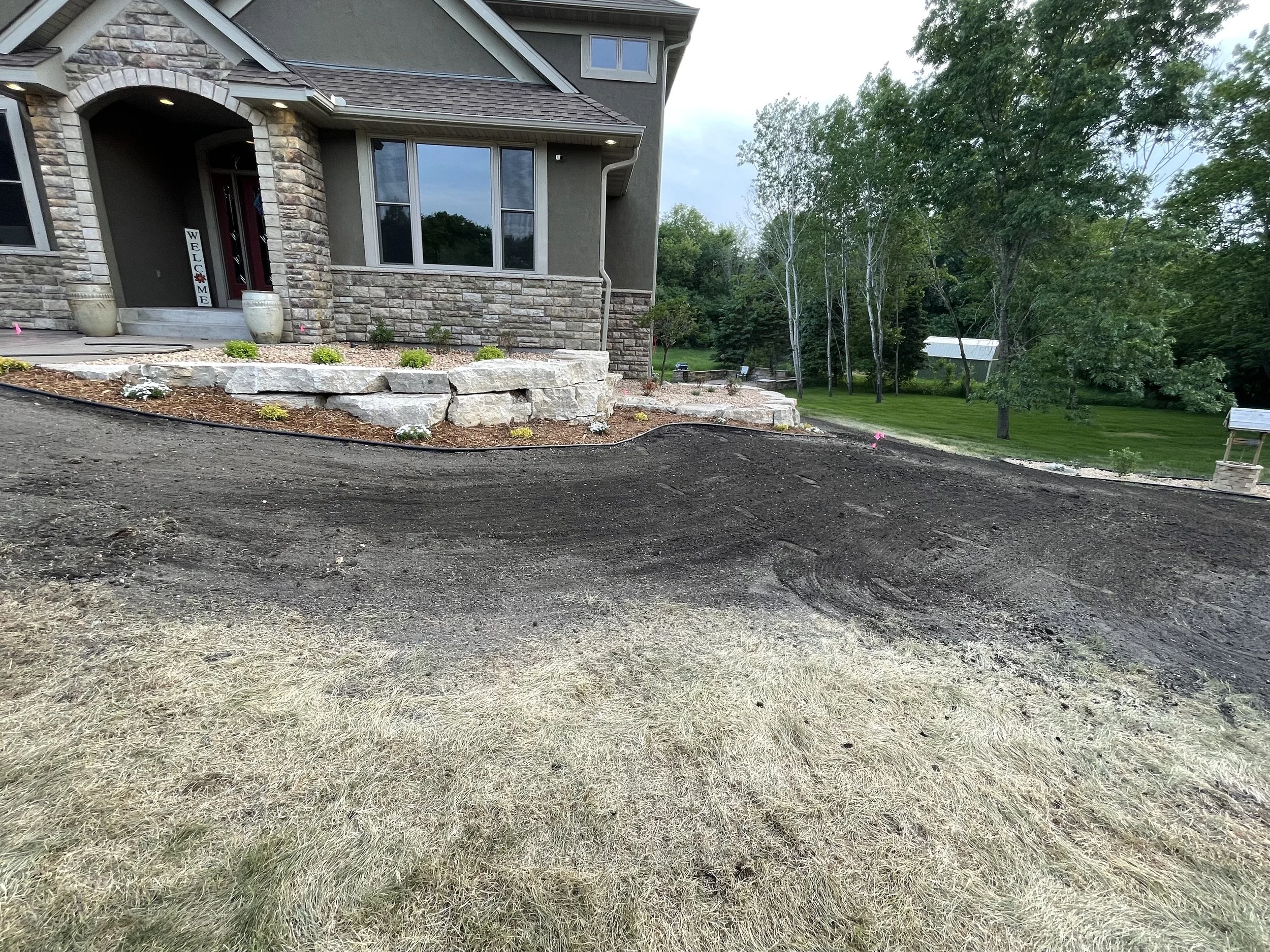 MB Landscapes installed landscaped yard with a natural stone wall and rock and mulch garden bed next to a house.
