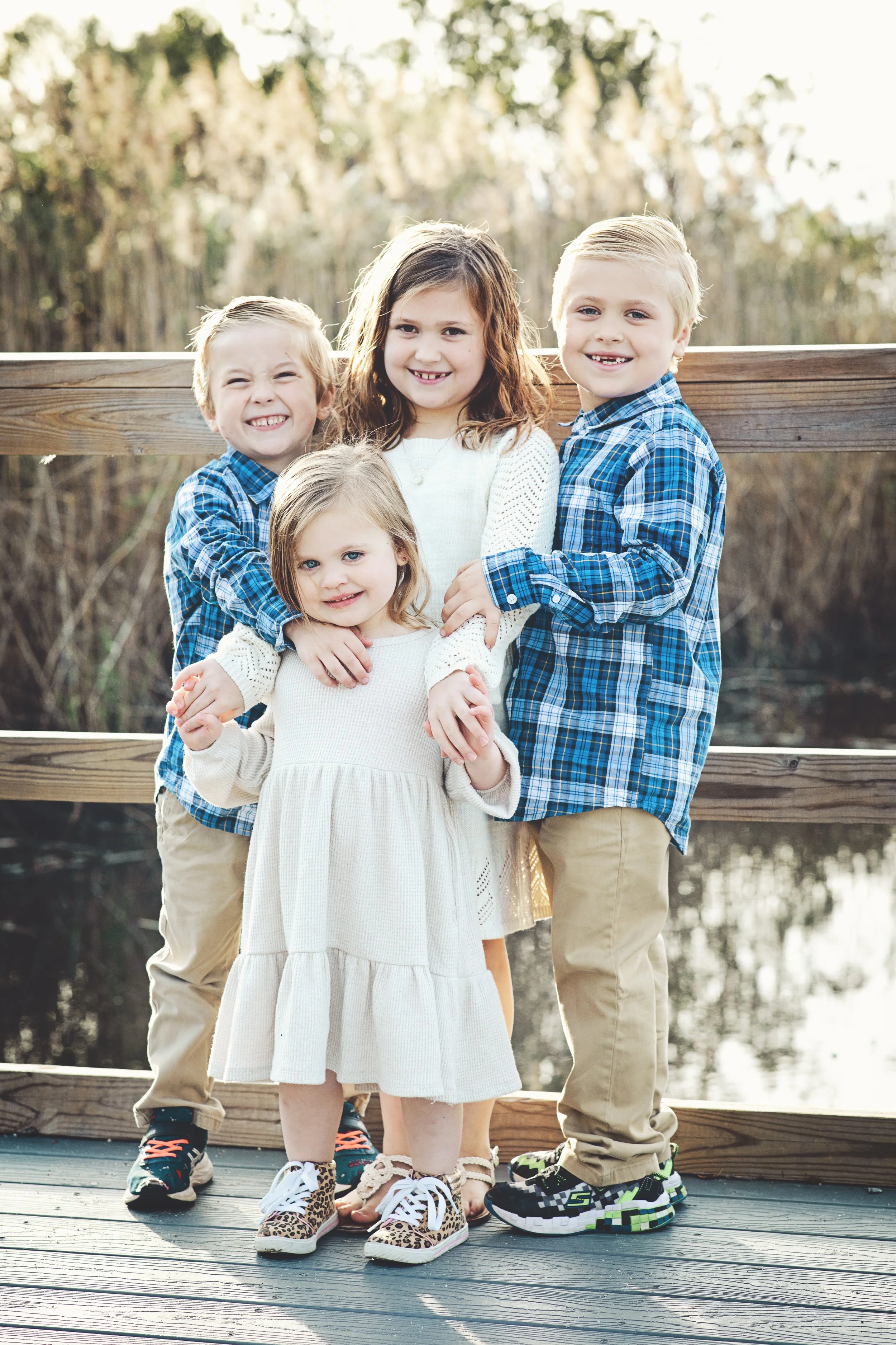 A group of five children standing on a wooden bridge outdoors with trees in the background, smiling at the camera.