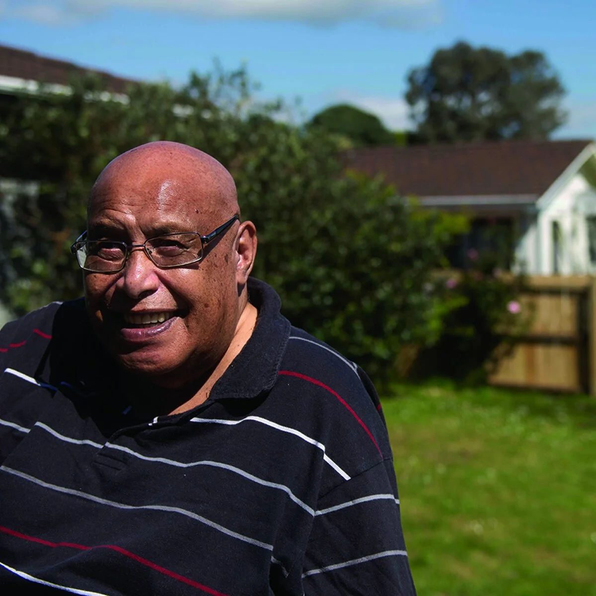 A Māori man, wearing glasses and a striped polo shirt, smiling at the camera.