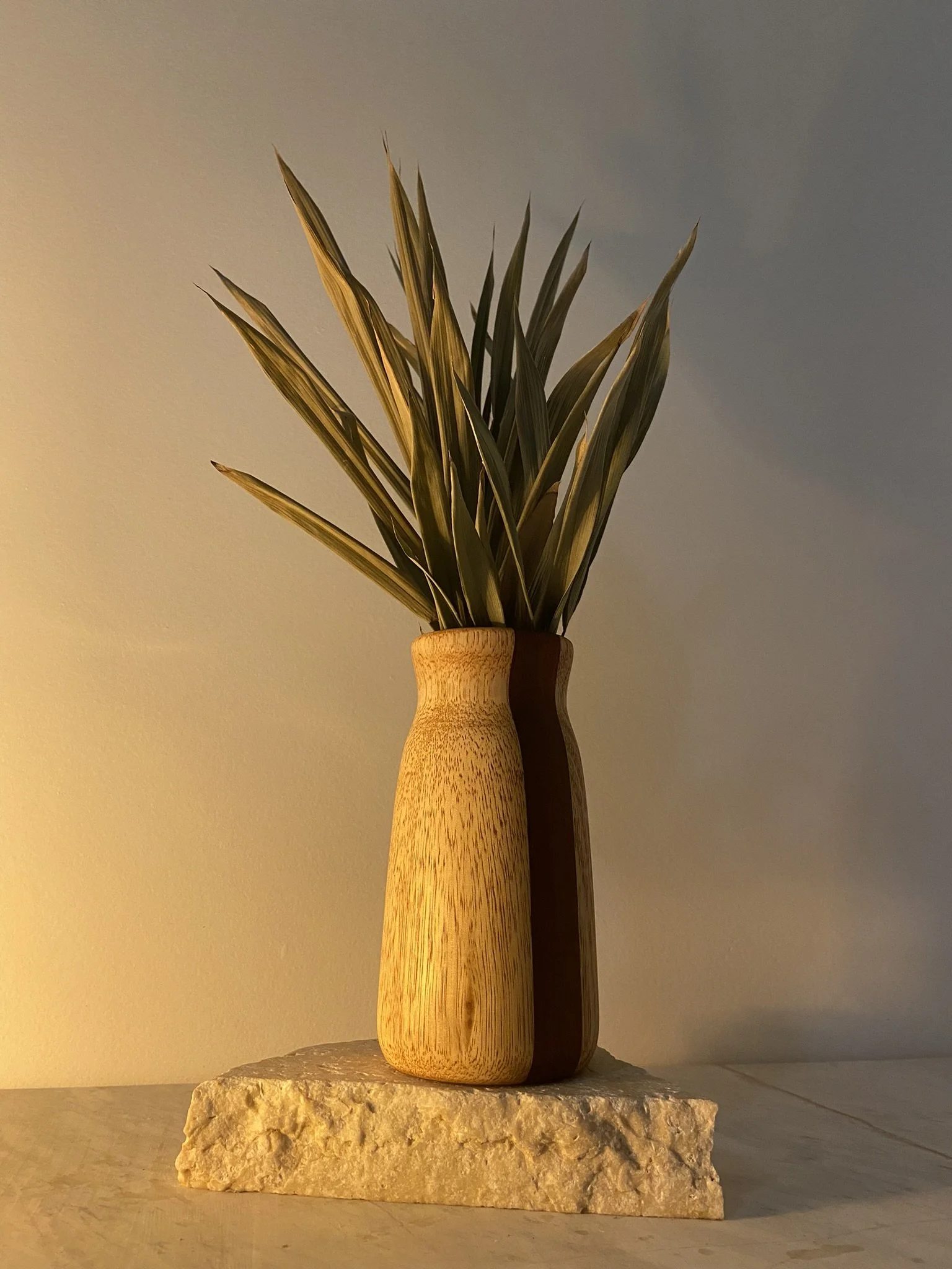 A decorative wooden vase with green leafy foliage, placed on a beige stone slab.