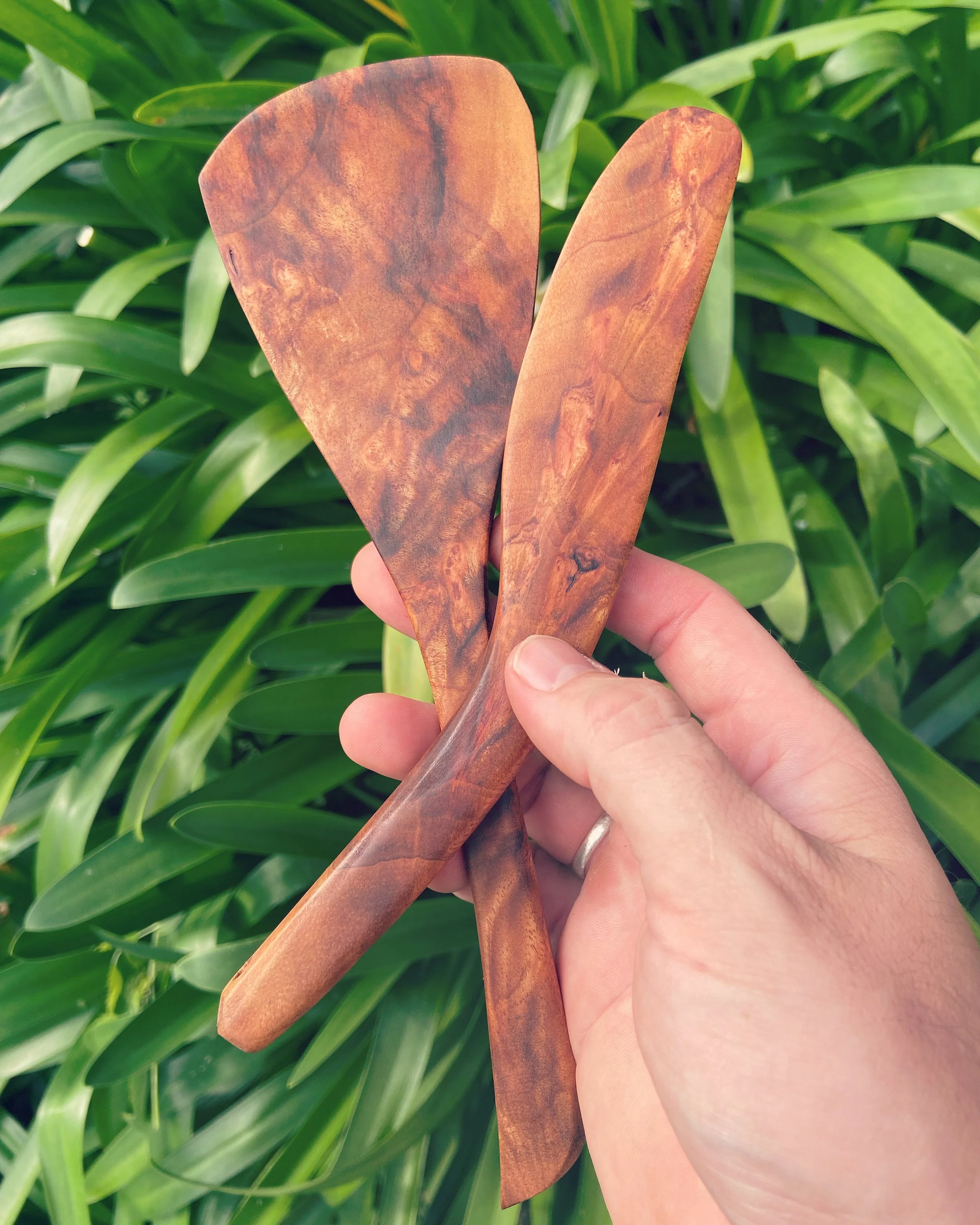 Person holding two wooden spatulas over green leafy plants