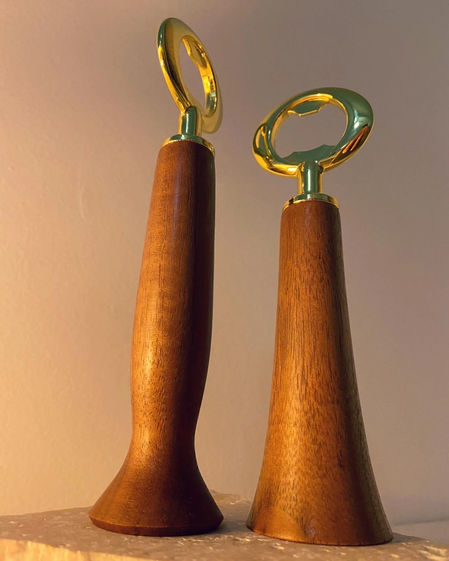 Two wooden-handled ice cream scoops with gold-colored metal handles standing on a surface against a plain background.