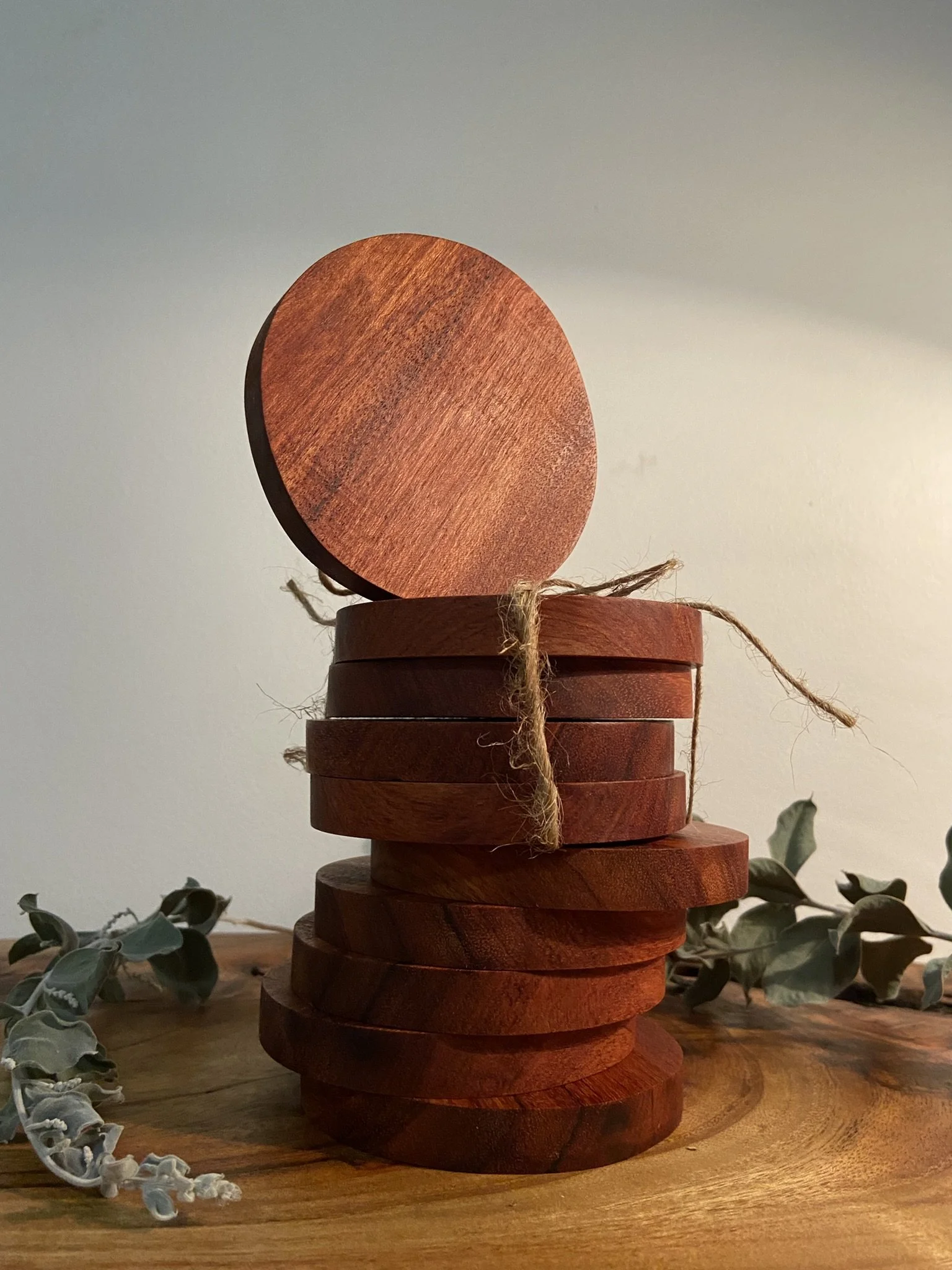 Stack of round wooden coasters tied with twine on a wooden surface with some dried leaves nearby.