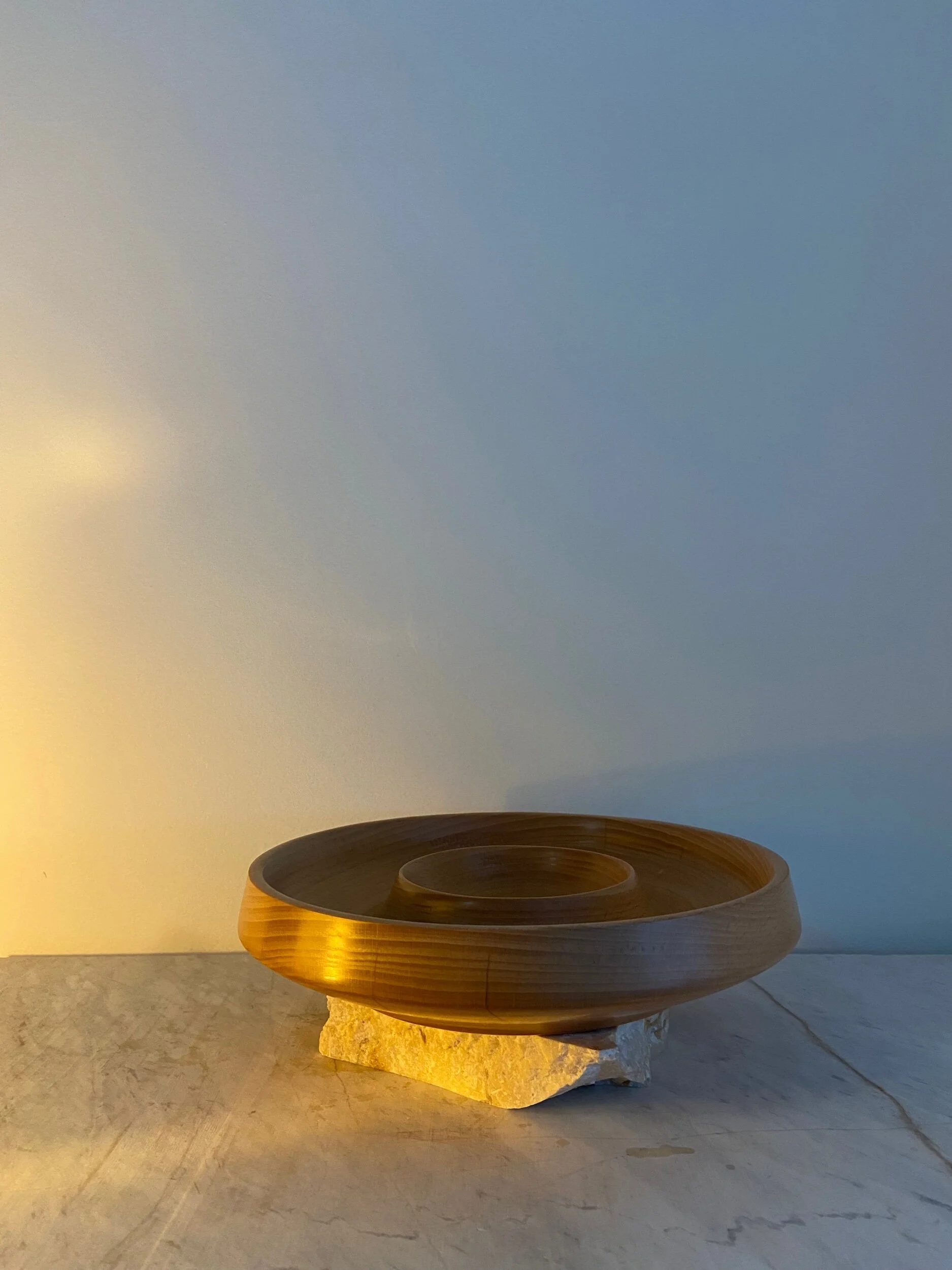 Decorative wooden bowl on a stone, illuminated by warm light, against a blue-gray wall.